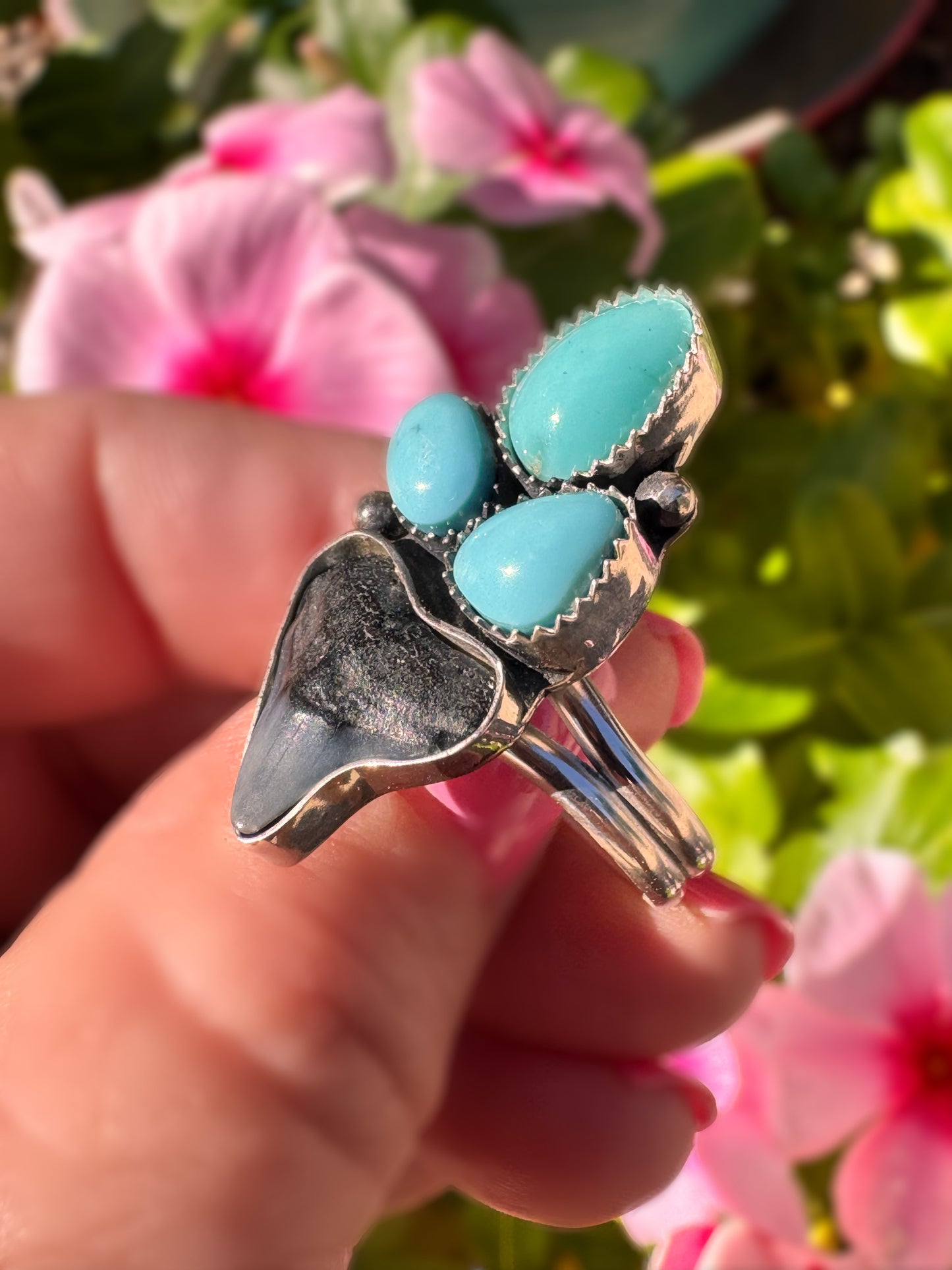 Silver ring with turquoise stones held in a hand against a floral background