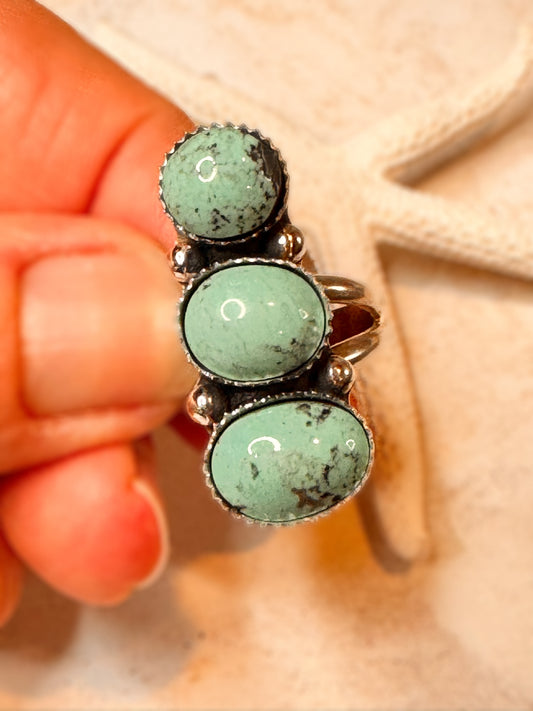 Turquoise stone ring held by a hand against a beige background