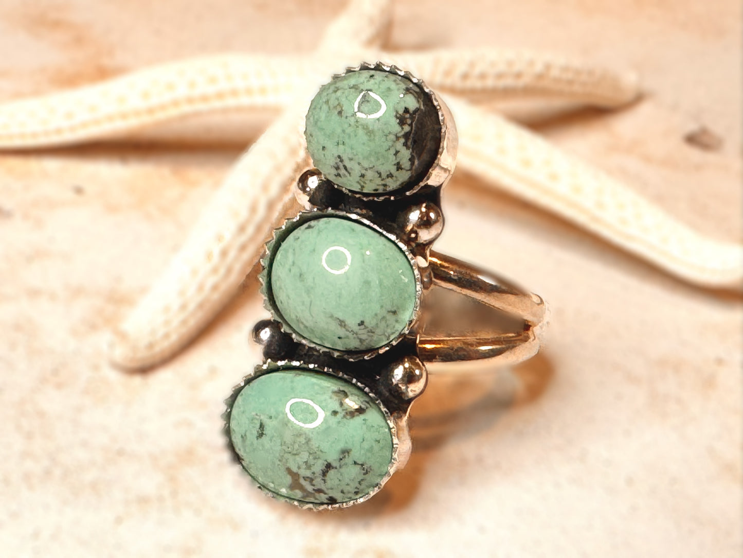 Ring with three green gemstones on a starfish and sand background