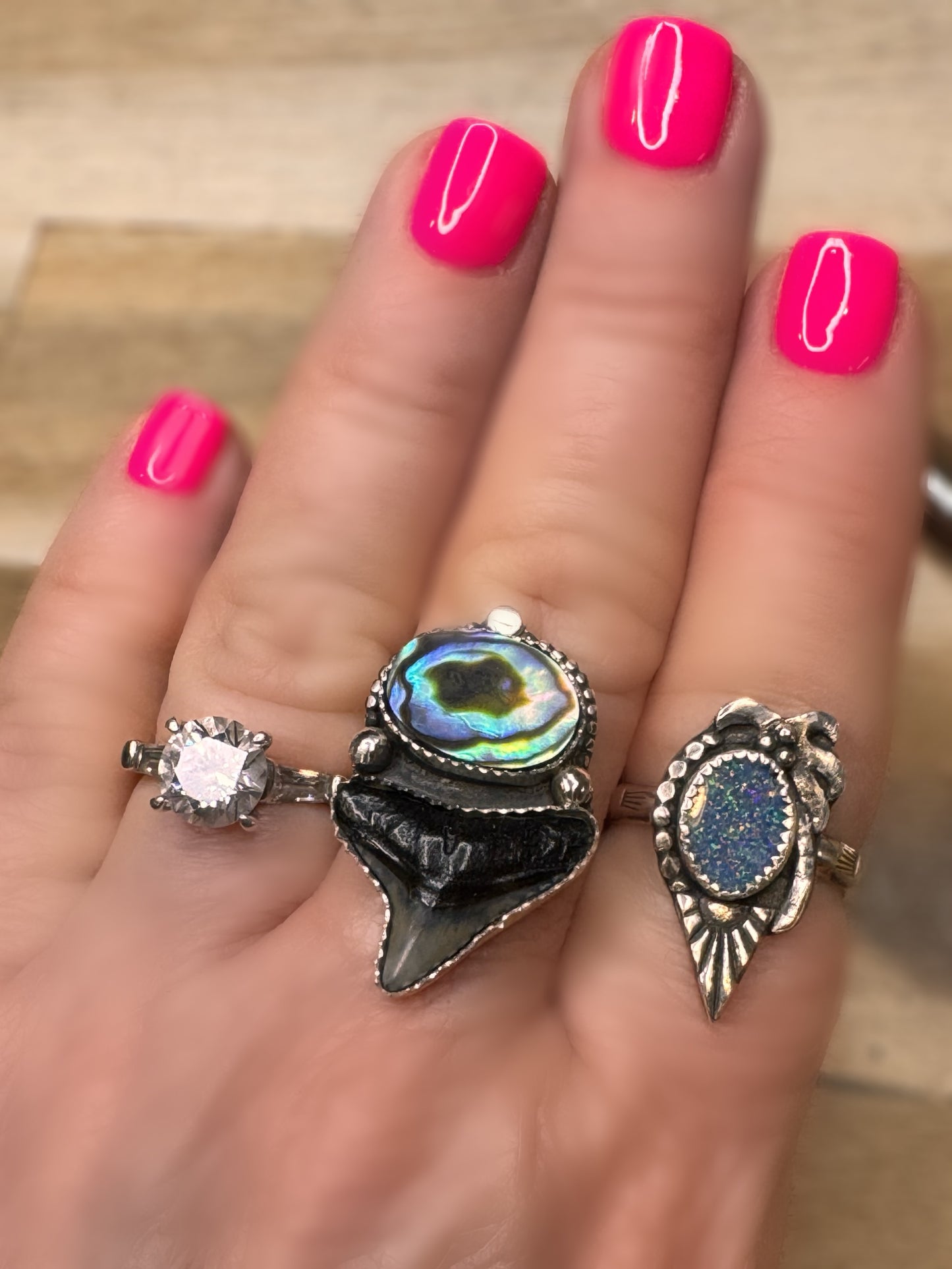 Abalone shell and shark tooth ring on a hand with pink nail polish on a neutral background