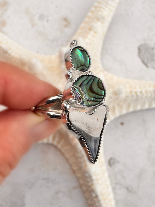 Silver ring with abalone shell on a finger against a natural background