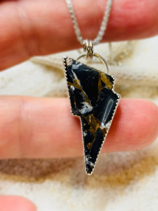 Lightning bolt pendant with black and gold pattern on a chain held between fingers.