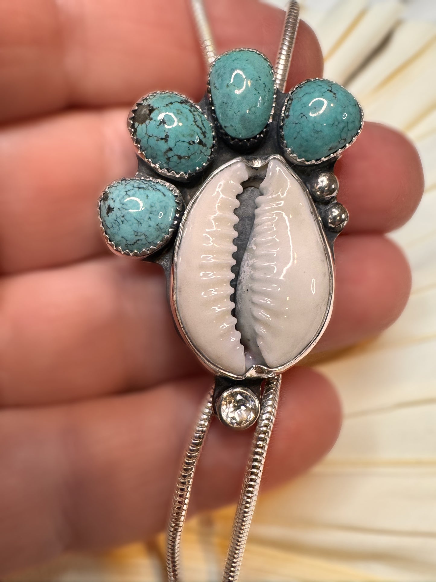 Handmade bolo necklace featuring cowrie shell, Fox turquoise, and white topaz in sterling silver, called Tidebearer.