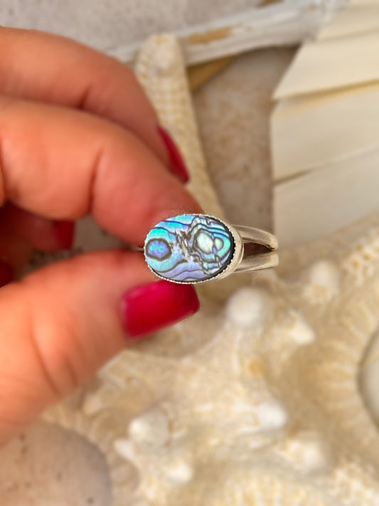 Close-up of a handcrafted abalone shell ring with iridescent blue and green hues, set in fine and sterling silver on a split shank band.