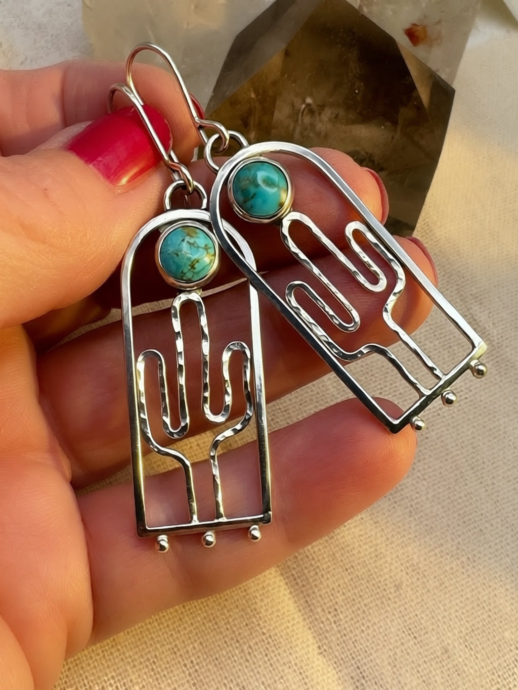 Hand-hammered sterling silver saguaro earrings with Blue Moon turquoise cabochons, approximately 2.5 inches, in hand