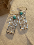 Hand-hammered sterling silver saguaro earrings with Blue Moon turquoise cabochons, approximately 2.5 inches, on a warm neutral background