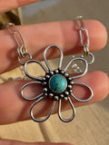 Silver flower-shaped pendant with turquoise center held between fingers