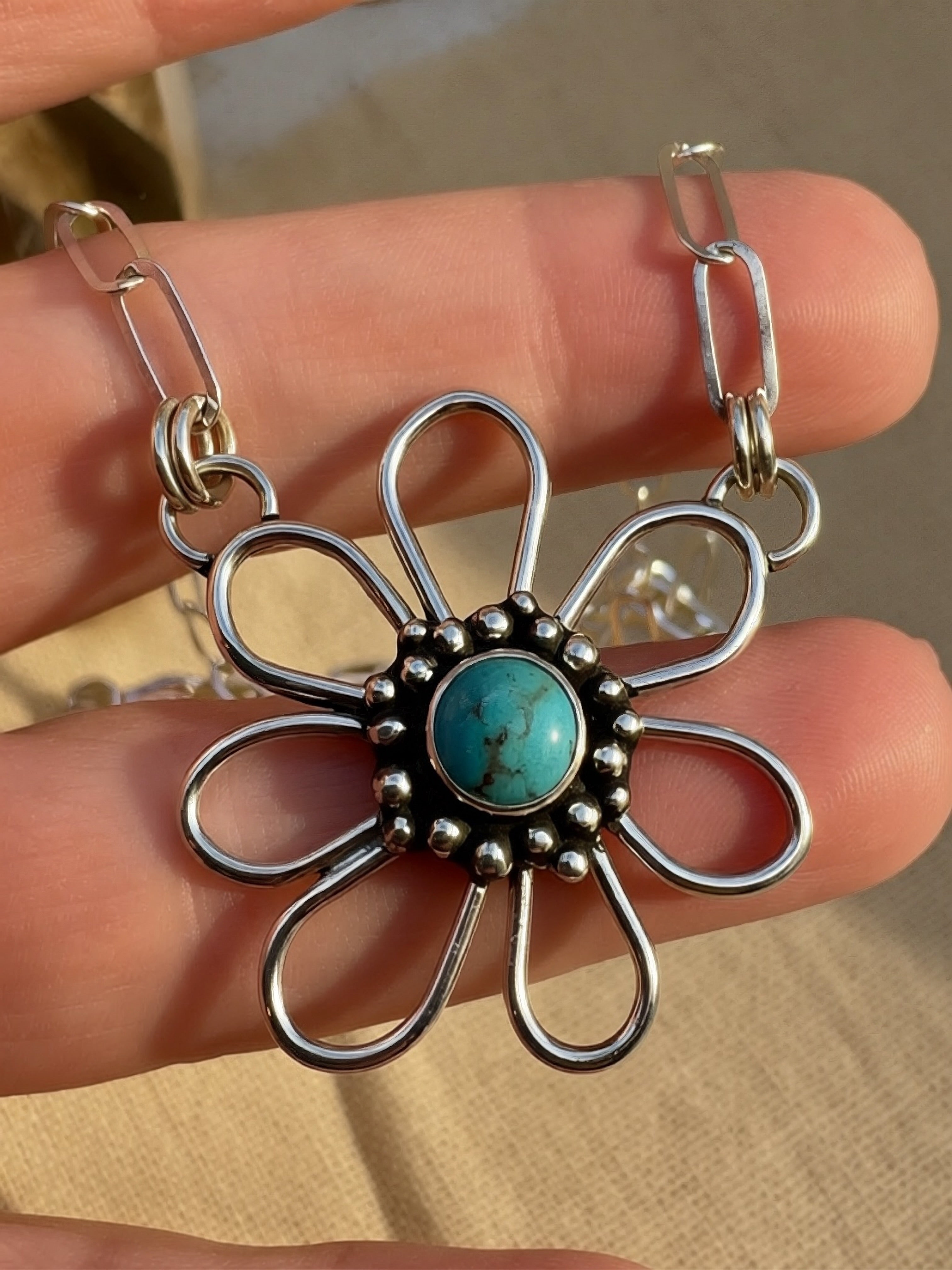 Silver flower-shaped pendant with turquoise center held between fingers