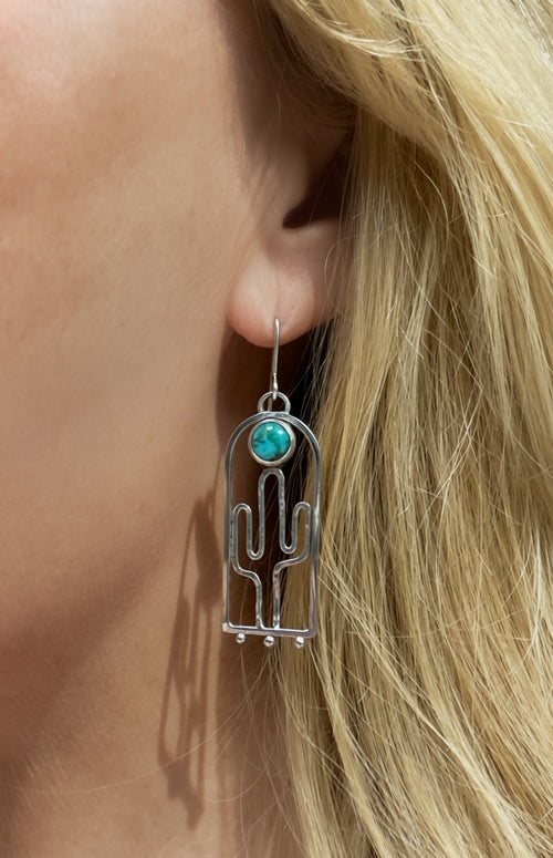 Hand-hammered sterling silver saguaro earrings with Blue Moon turquoise cabochons, approximately 2.5 inches, being worn