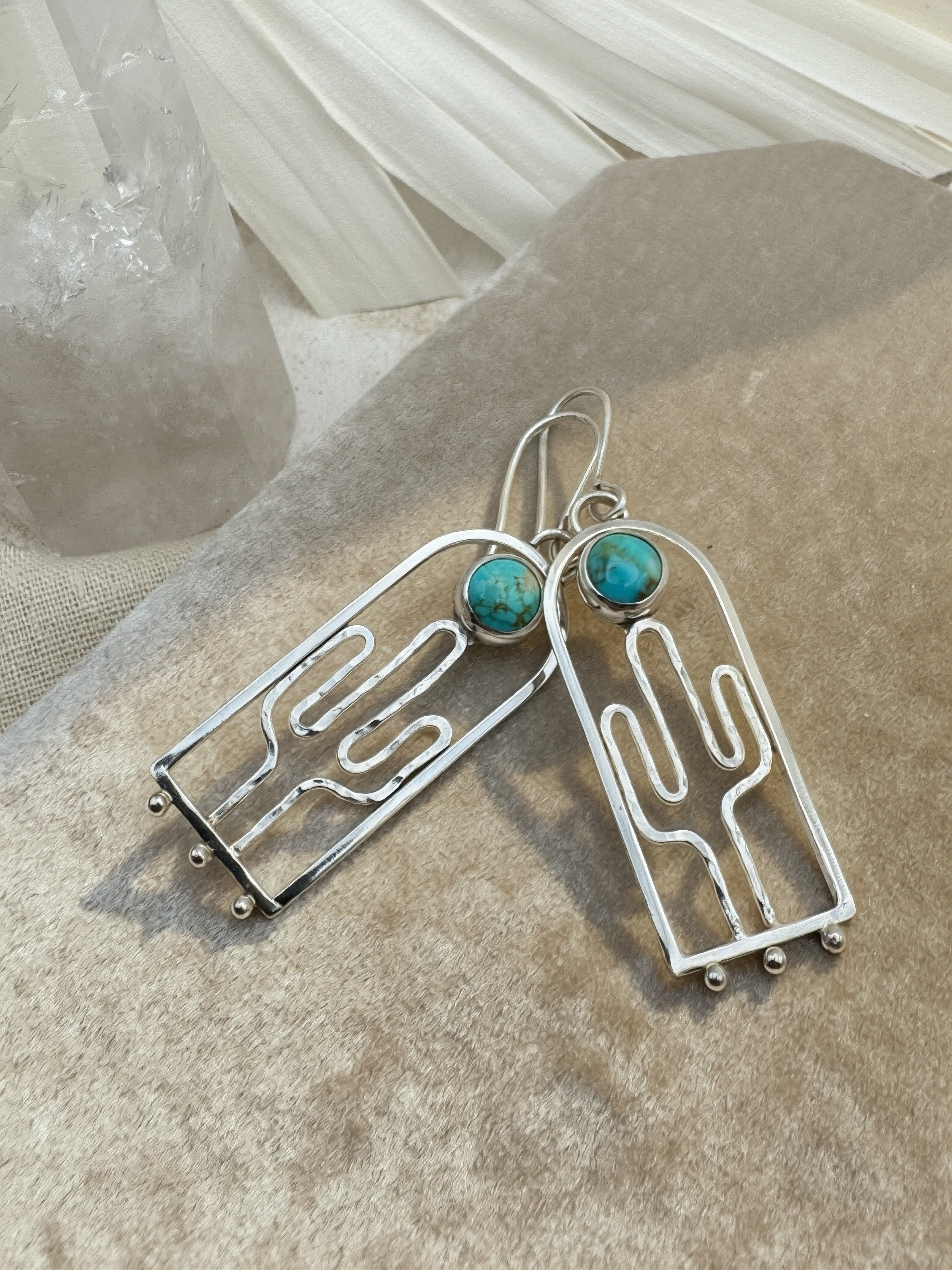 Hand-hammered sterling silver saguaro earrings with Blue Moon turquoise cabochons, approximately 2.5 inches, on a warm neutral background