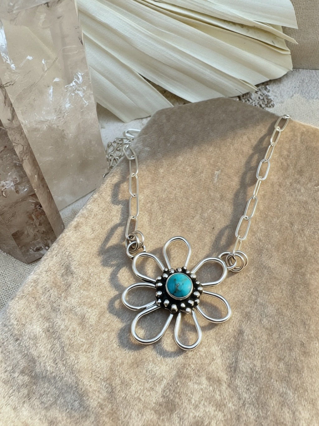 Silver necklace with a flower-shaped pendant featuring a sleeping beauty turquoise stone on a stone surface.