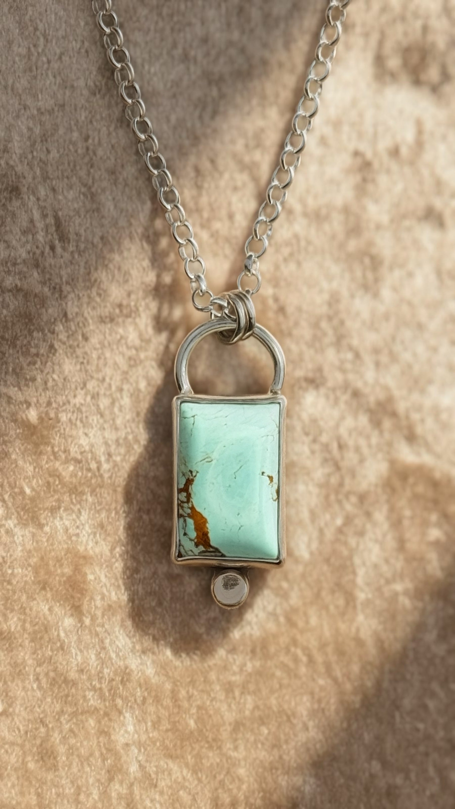 Necklace with a rectangular turquoise pendant on a textured beige background