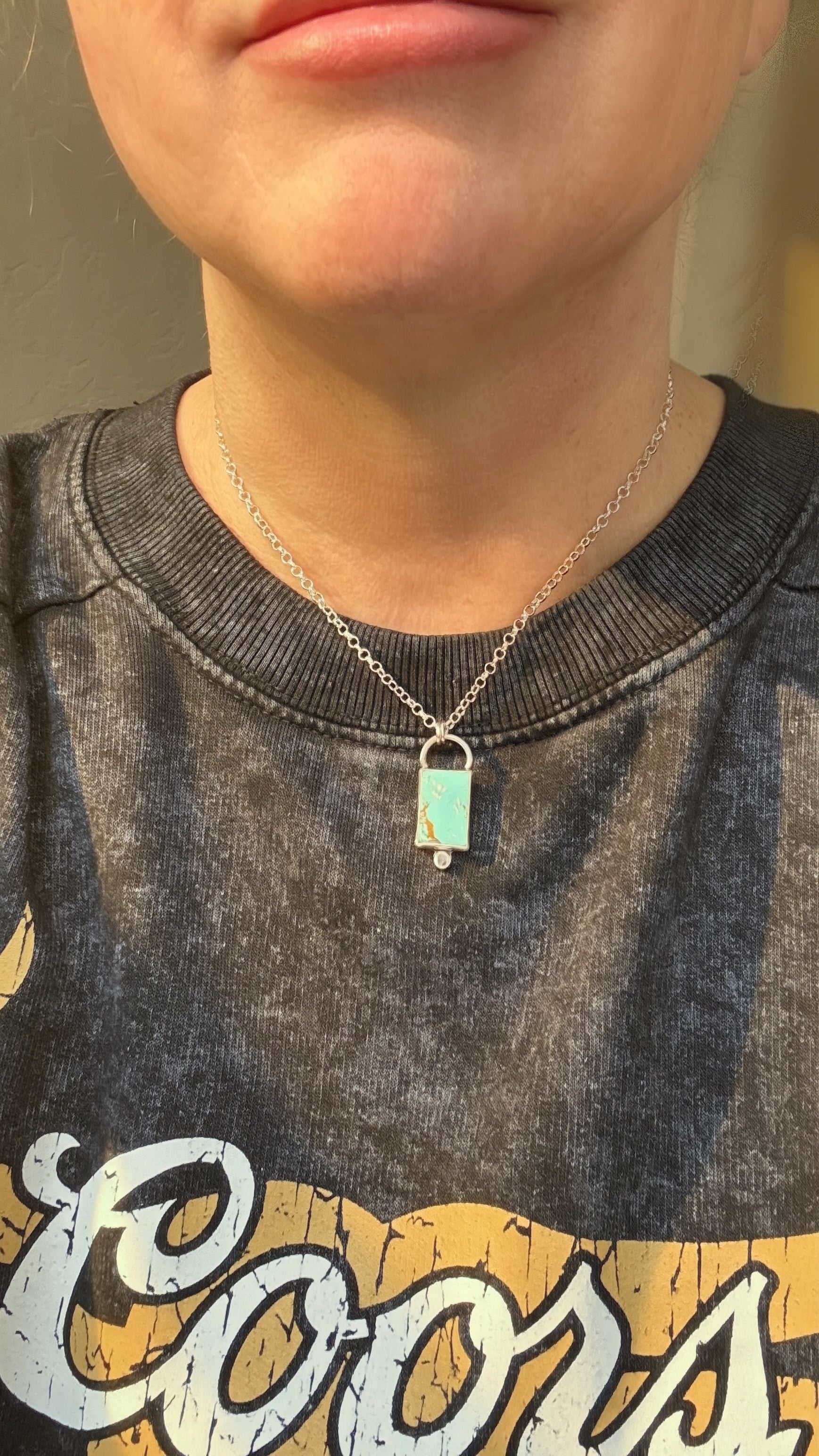 Person wearing a necklace with a pendant, against a neutral background