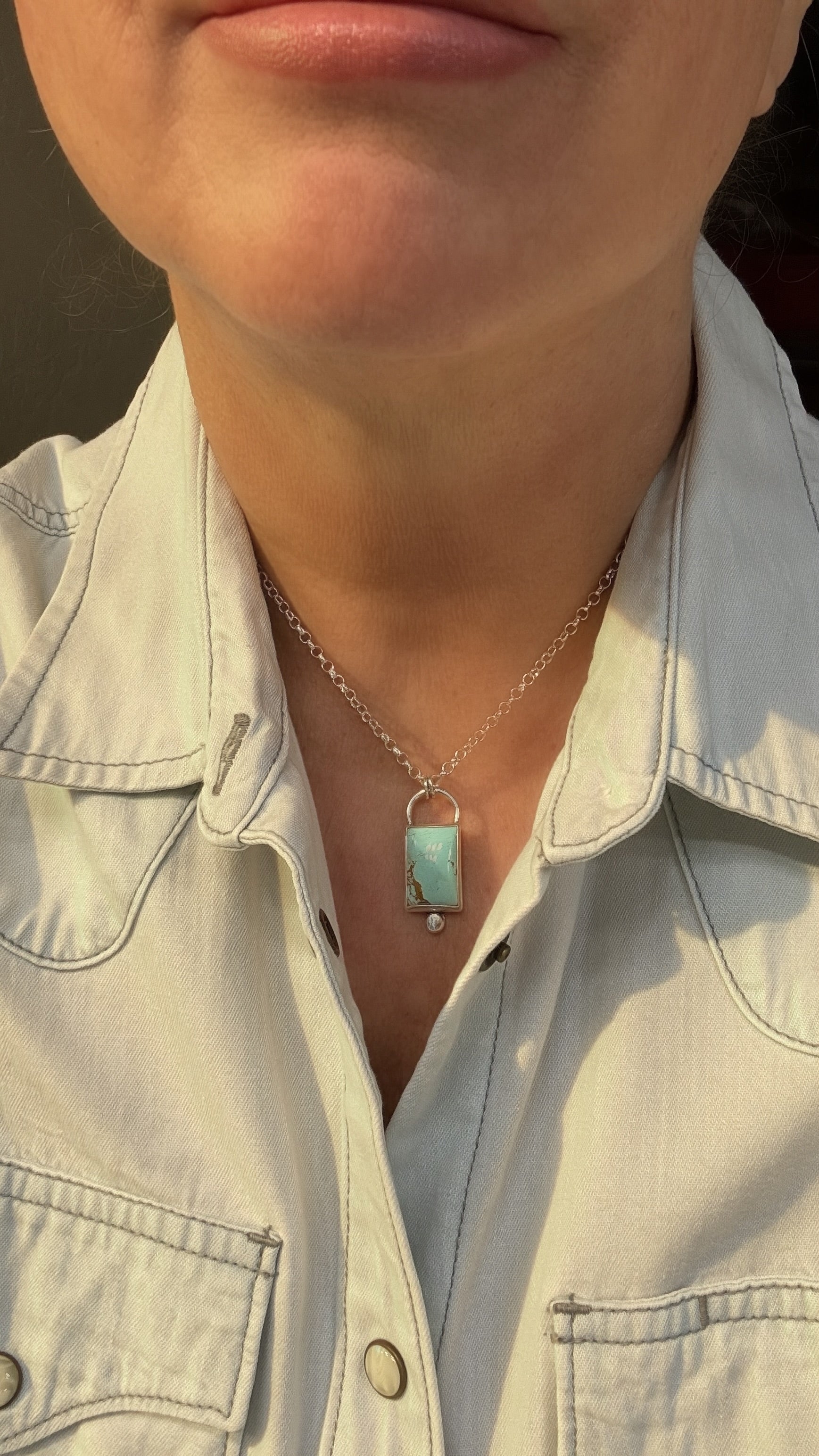 Necklace with a turquoise pendant worn by a person in a light-colored shirt.