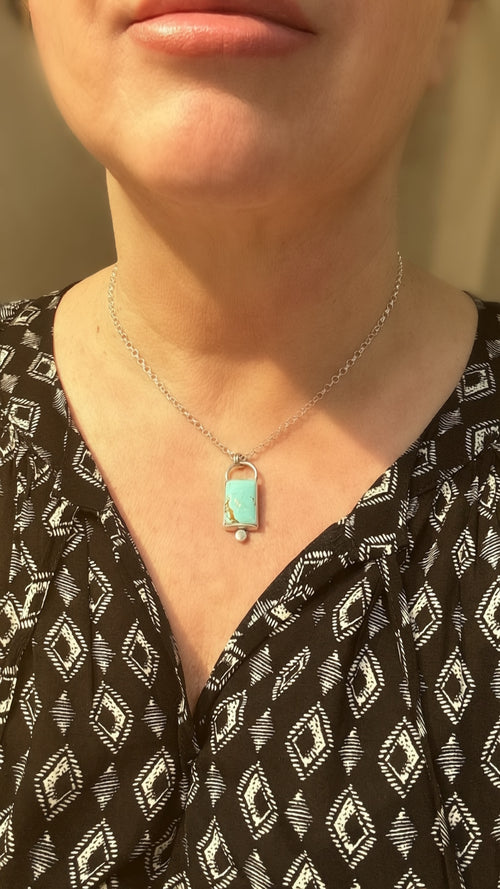 Necklace with a turquoise pendant worn by a person in a black patterned top.