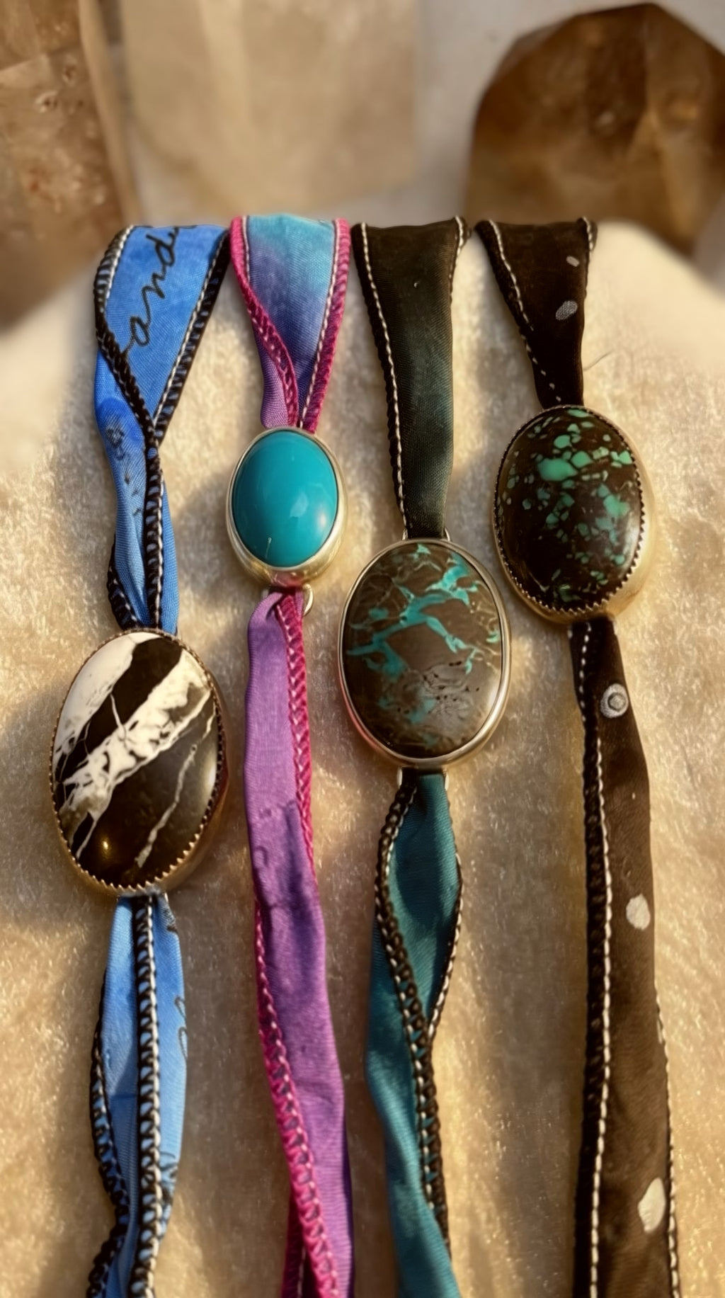 Four colorful bolo ties with decorative stones on a textured surface
