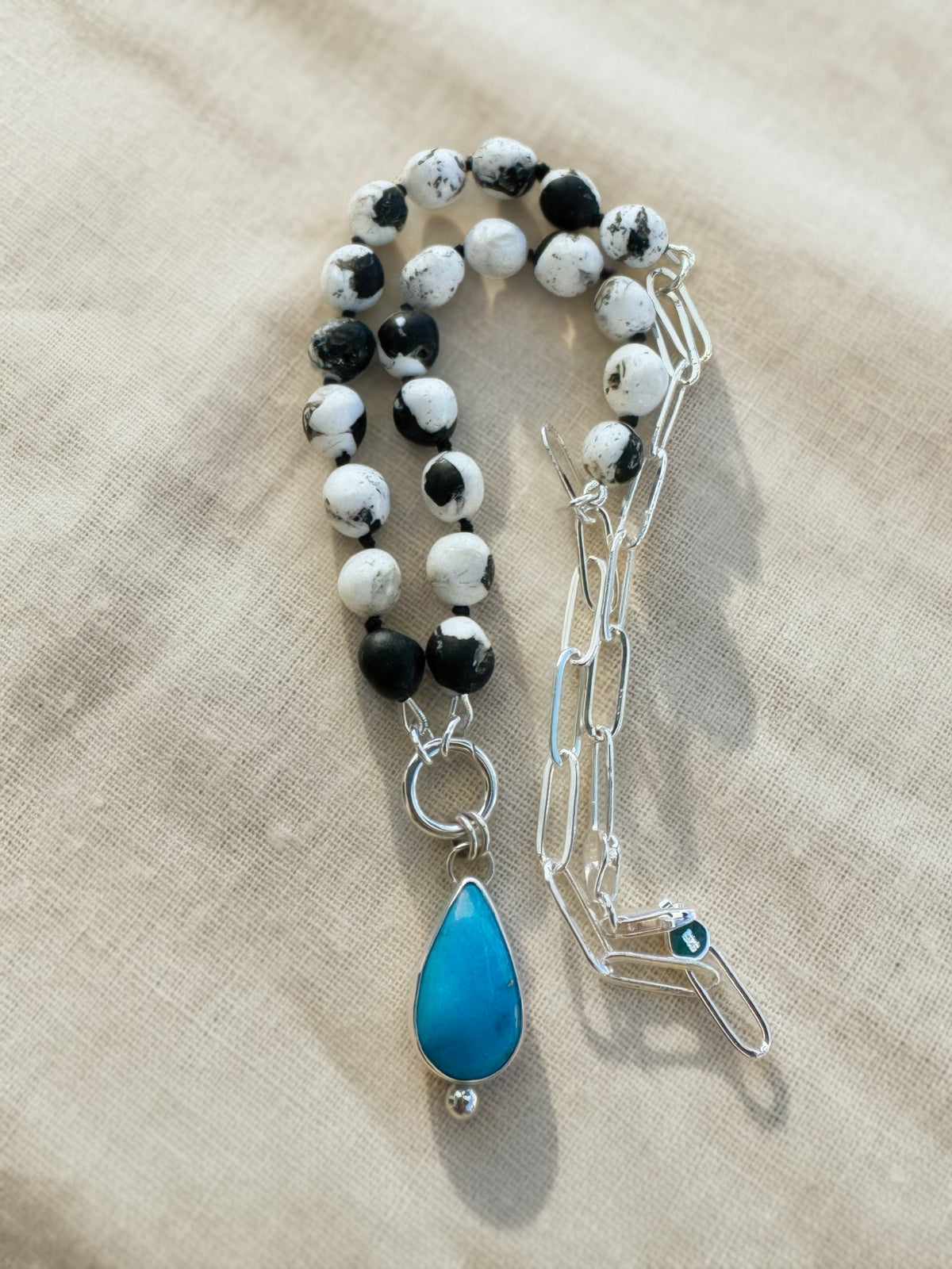 Full Blue Meridian necklace on beige fabric, showing composite White Buffalo beads, sterling paperclip chain, and a turquoise pendant.