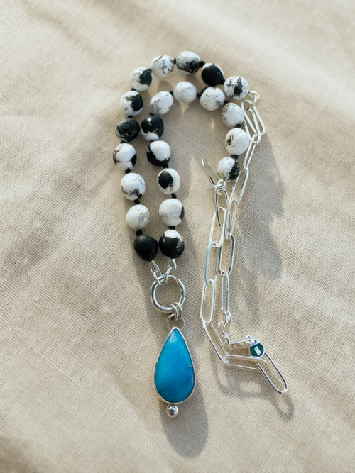 Full Blue Meridian necklace on beige fabric, showing composite White Buffalo beads, sterling paperclip chain, and a turquoise pendant.