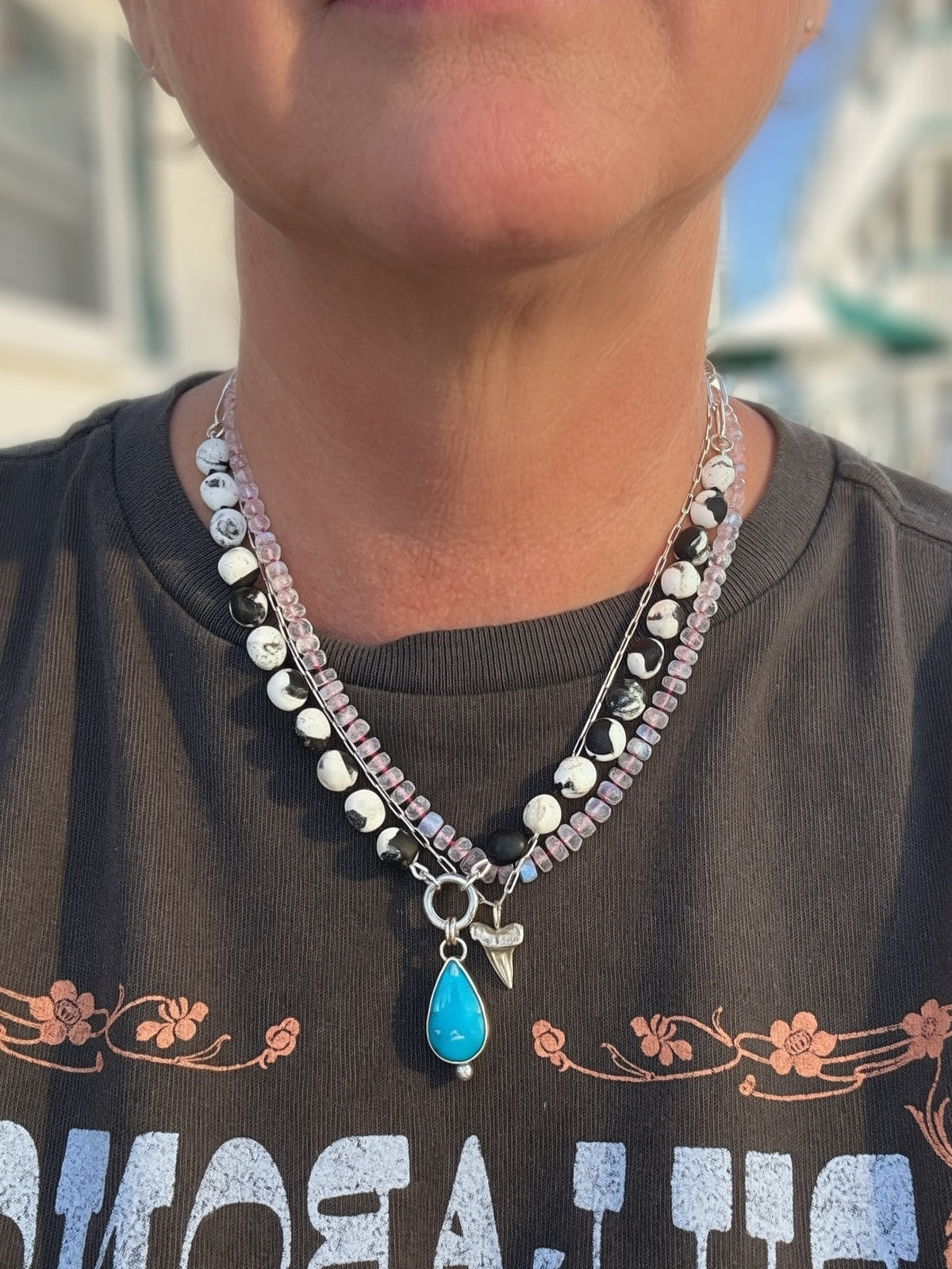 Blue Meridian turquoise and composite White Buffalo necklace worn with a separate pale-pink beaded strand and silver shark tooth charm.