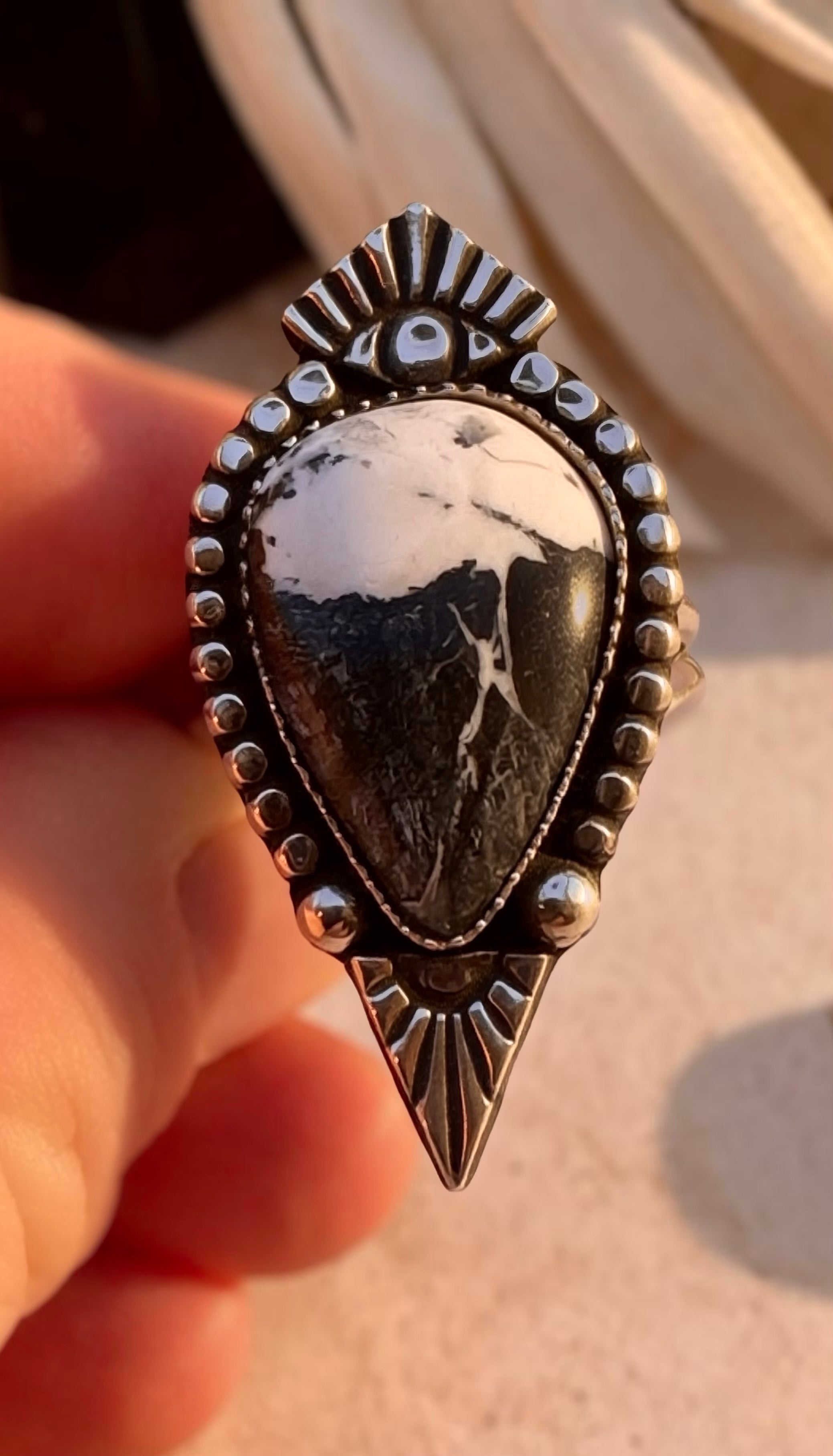 Silver ring with a white buffalo stone held by a hand on a neutral background