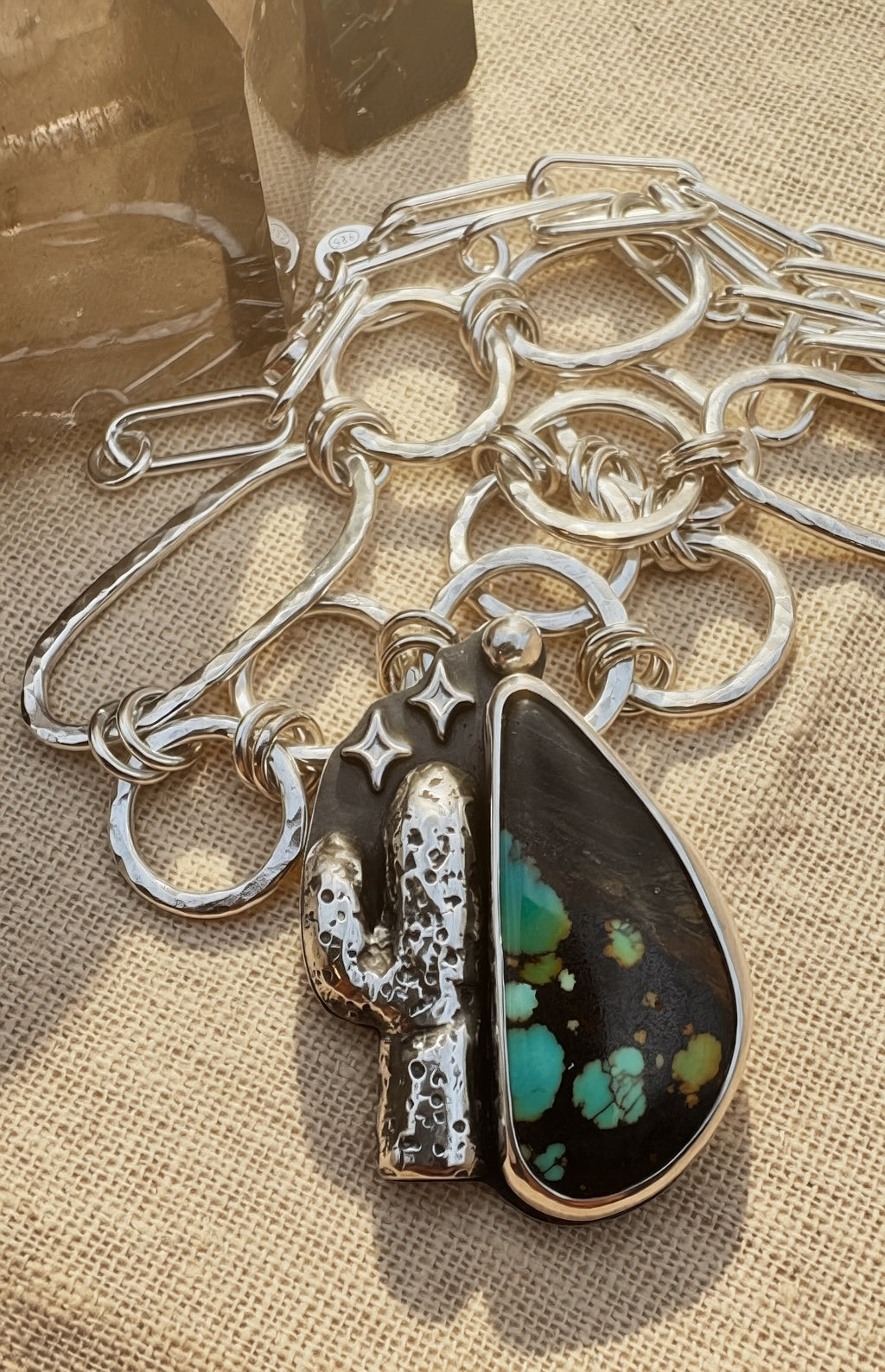 Silver Necklace with a saguaro and a teardrop-shaped hubei turquoise on a textured surface.