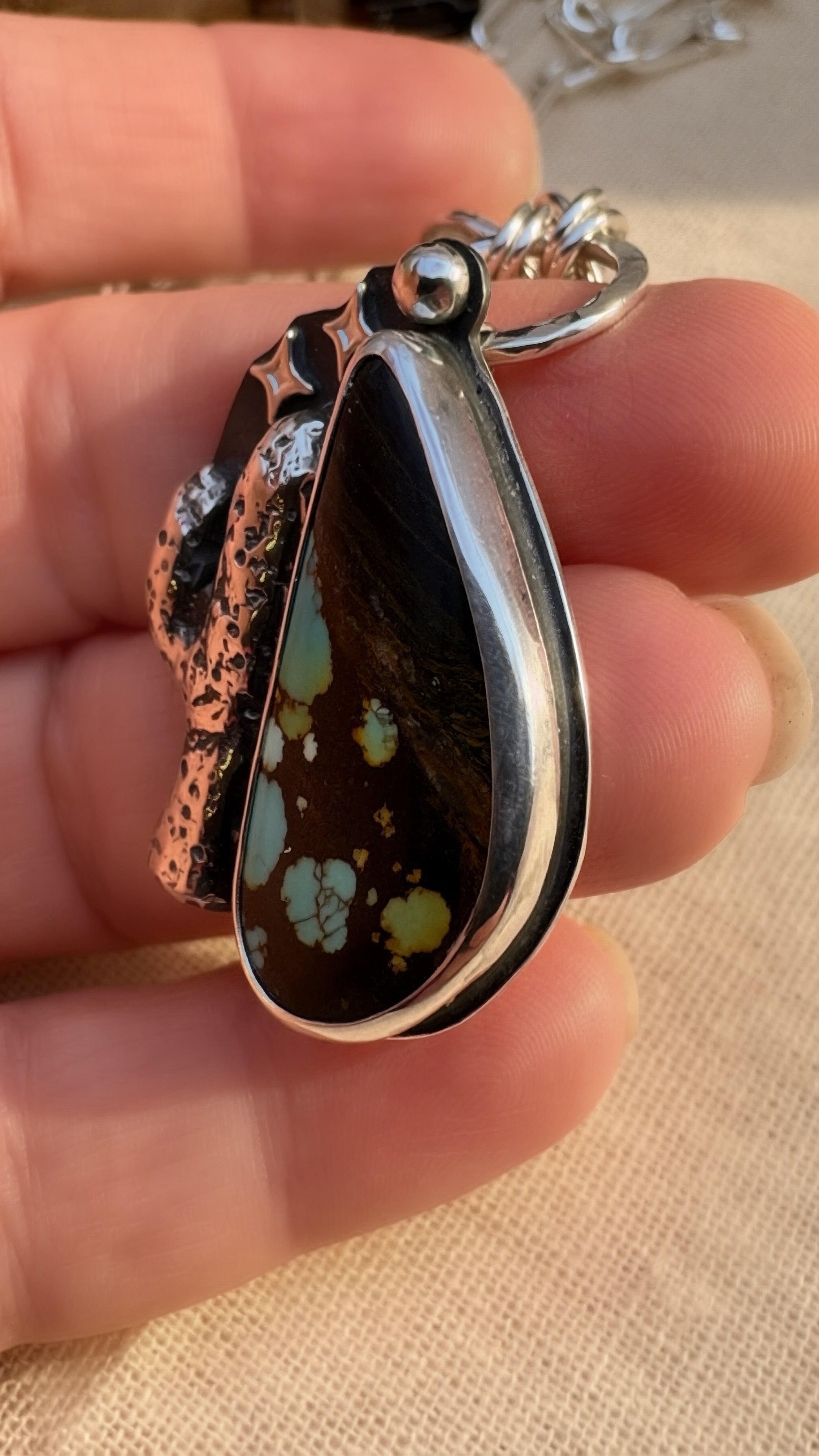 Teardrop-shaped pendant turquoise and silver held in a hand to display the bezel 