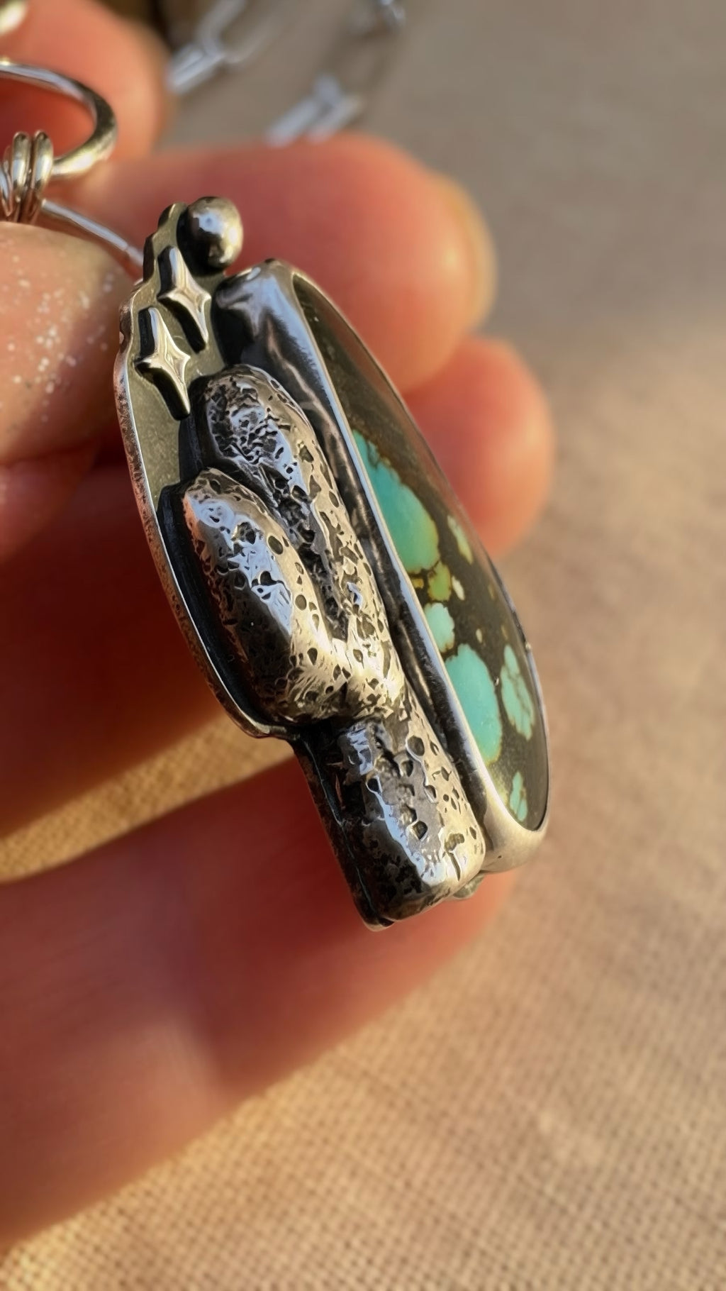 Close-up side view of a silver pendant with a saguaro and Hubei turquoise held in a hand.