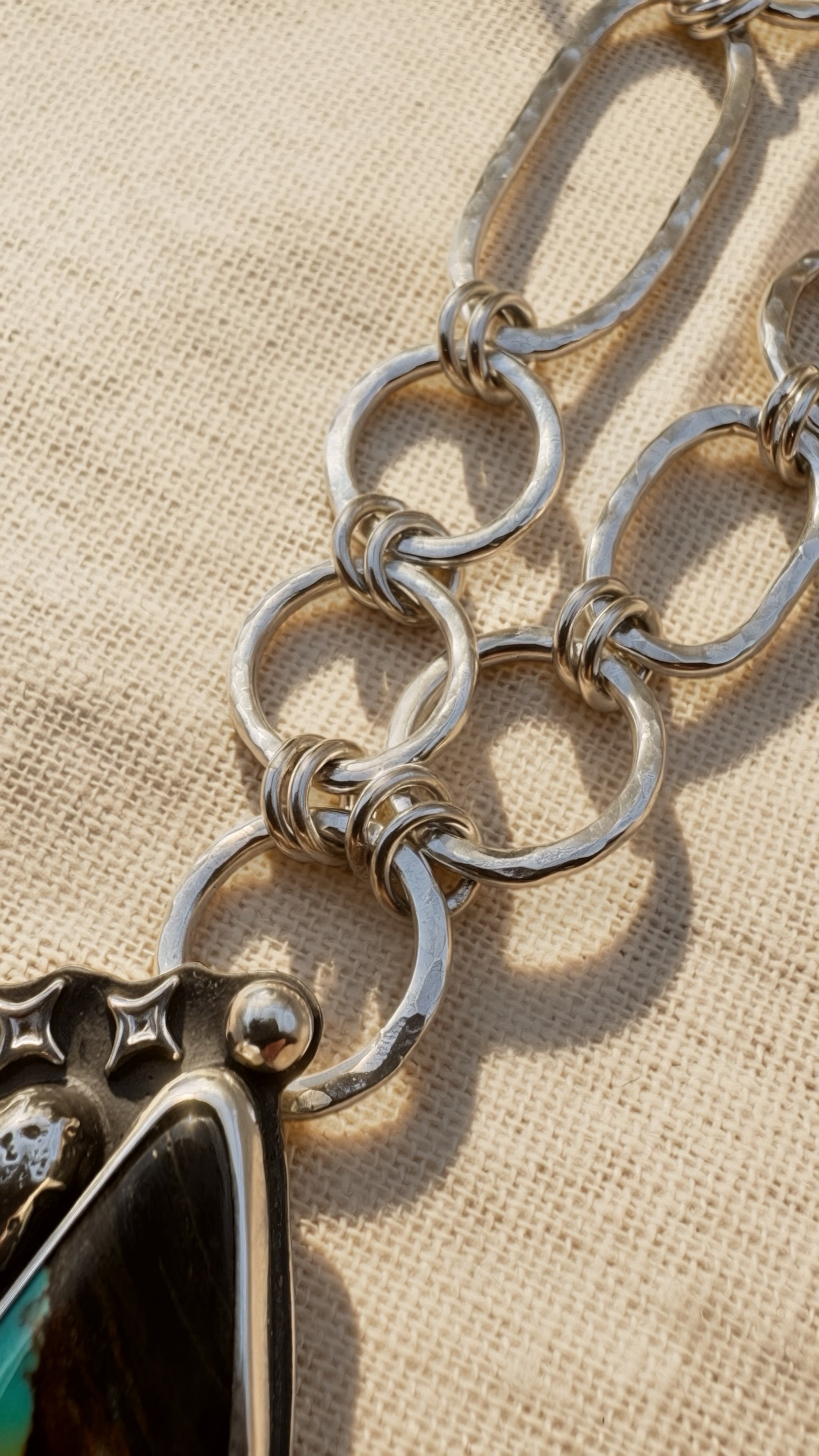 Close-up of a hubei turquoise and silver chain necklace with a textured beige background