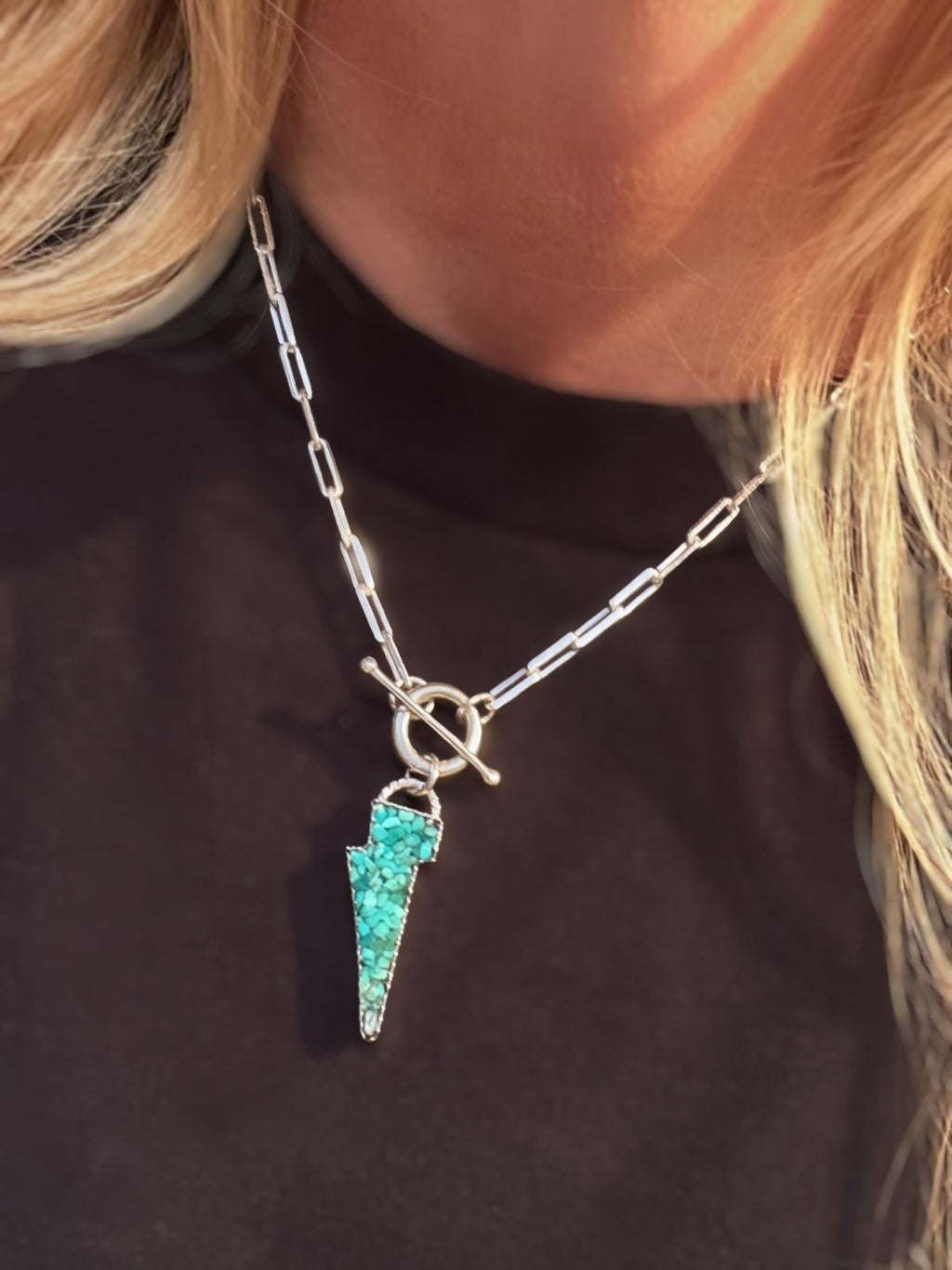 Lightning bolt pendant with Kingman turquoise inlay on a paperclip toggle chain, against a black tee.
