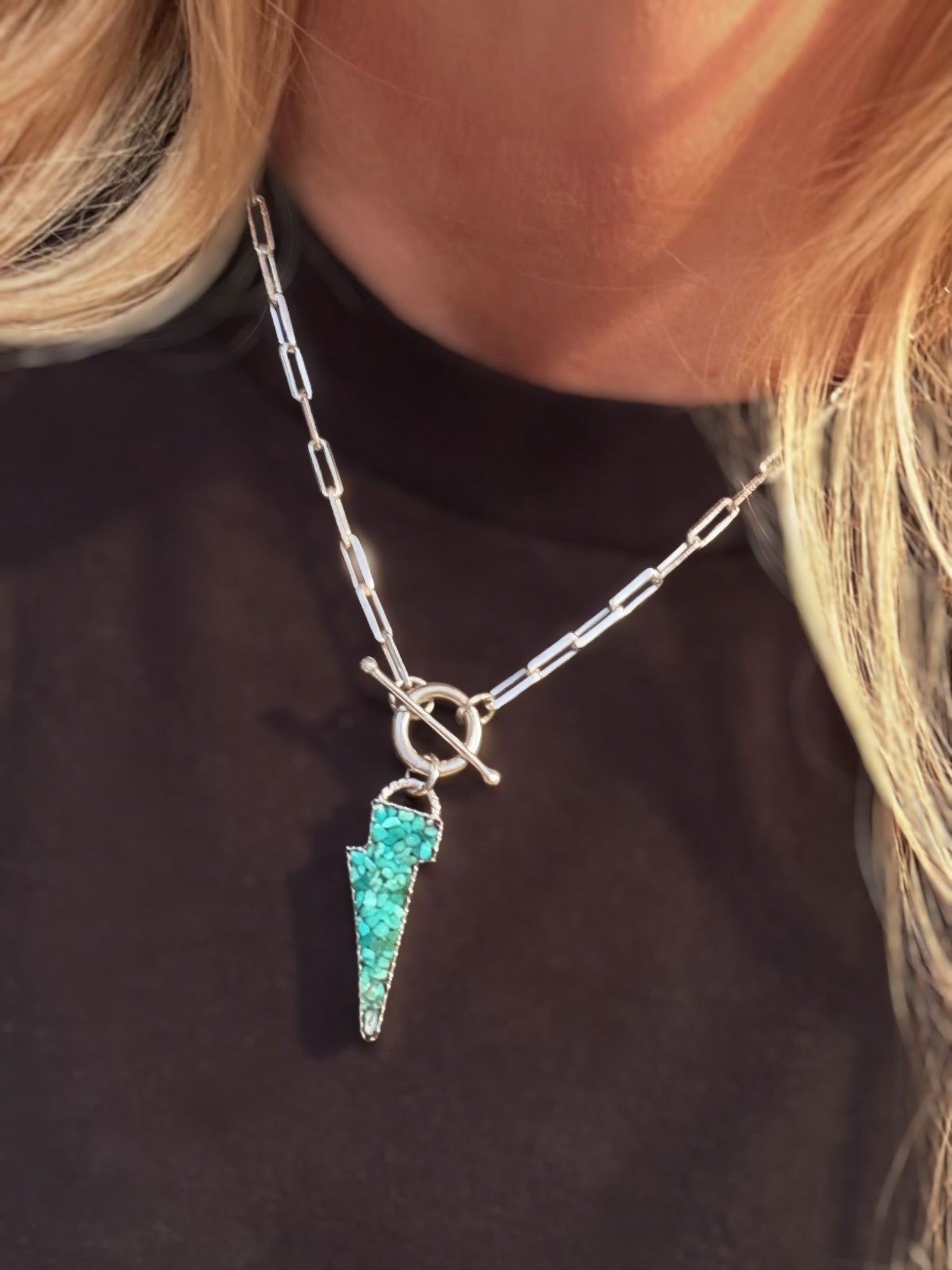 Lightning bolt pendant with Kingman turquoise inlay on a paperclip toggle chain, against a black tee.