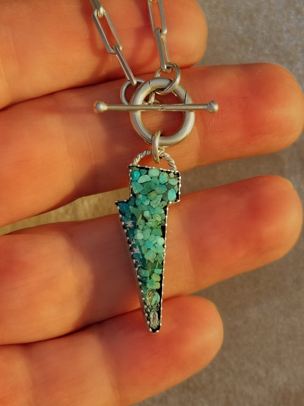 Lightning bolt pendant with Kingman turquoise inlay on a paperclip toggle chain, being hand held.