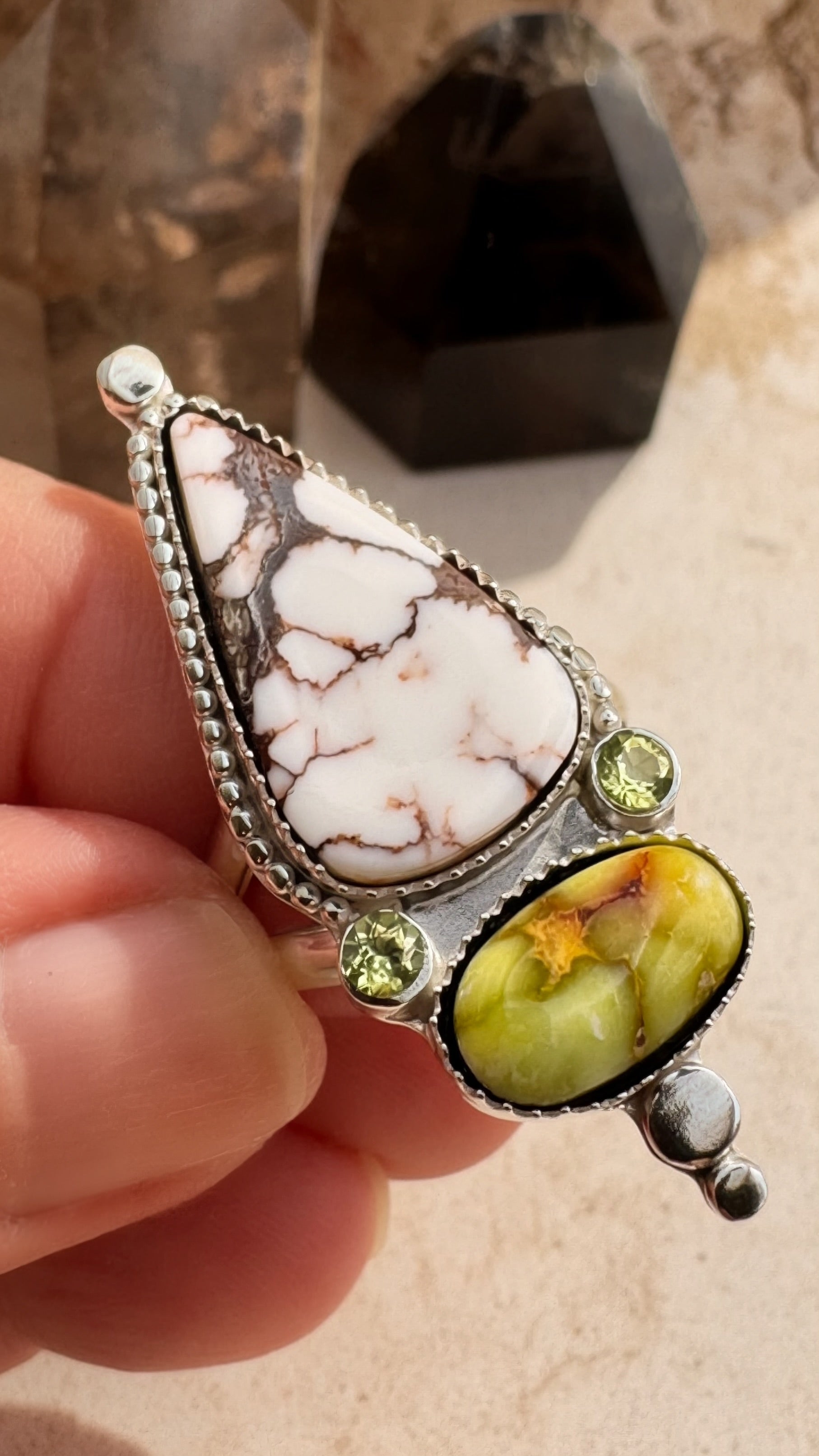 Jewelry with white stone and green gemstone held in a hand against a neutral background