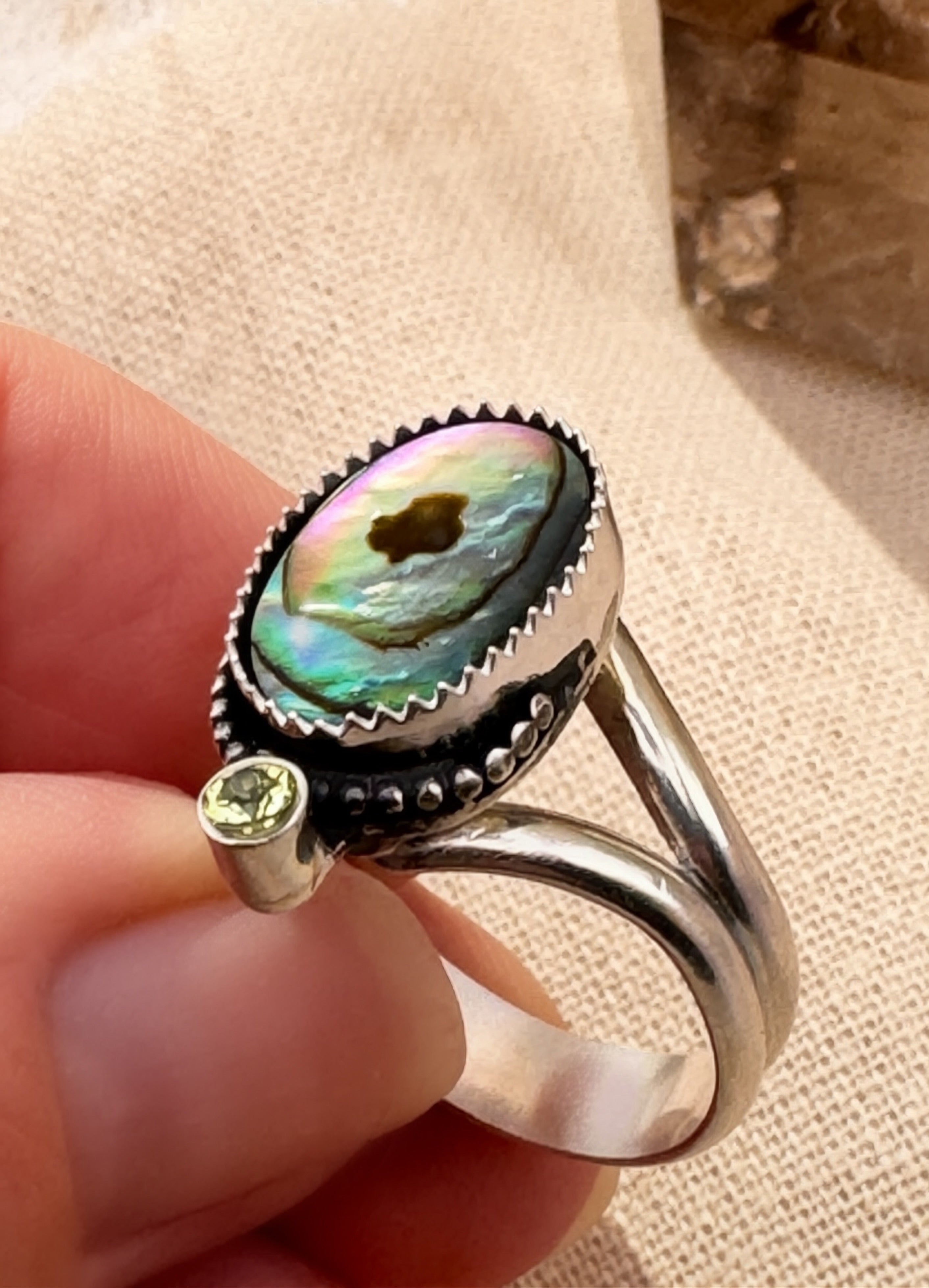 Iridescent abalone shell ring with faceted peridot and bead wire detail