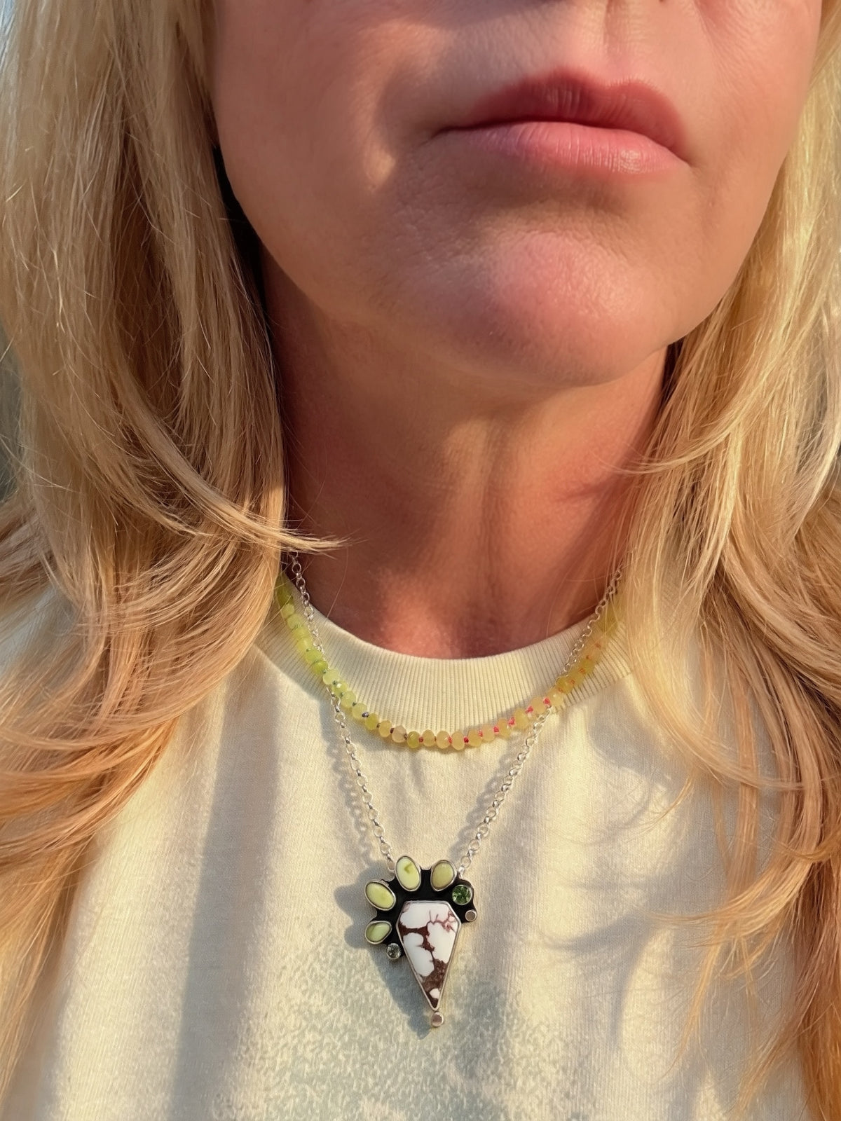 Blonde woman wearing a Wild horse and variscite pendant in sterling silver with peridot accents, handcrafted one-of-a-kind necklace. Wild horse stone is shaped like a diamond with the varisicte and palomino stones accenting the shape.