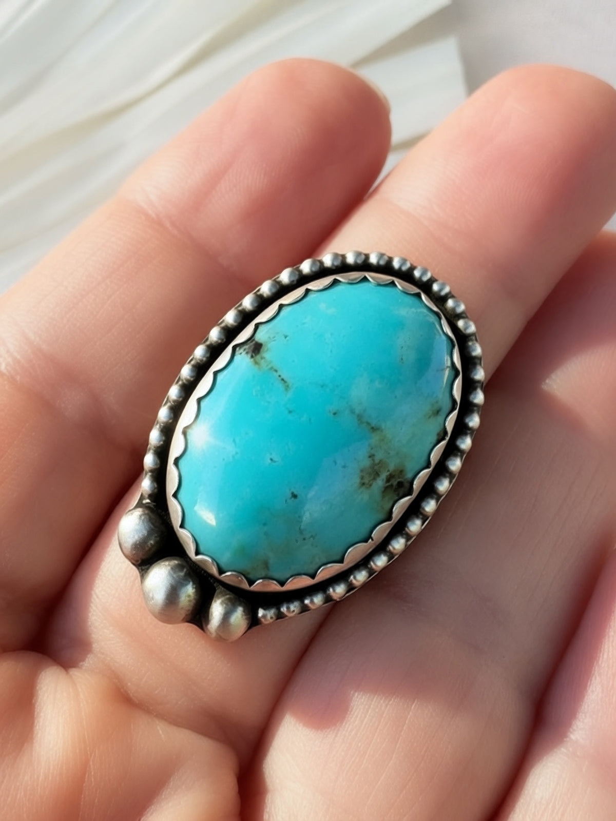 A sterling silver ring with an oval turquoise stone, shown resting on a person's fingers.