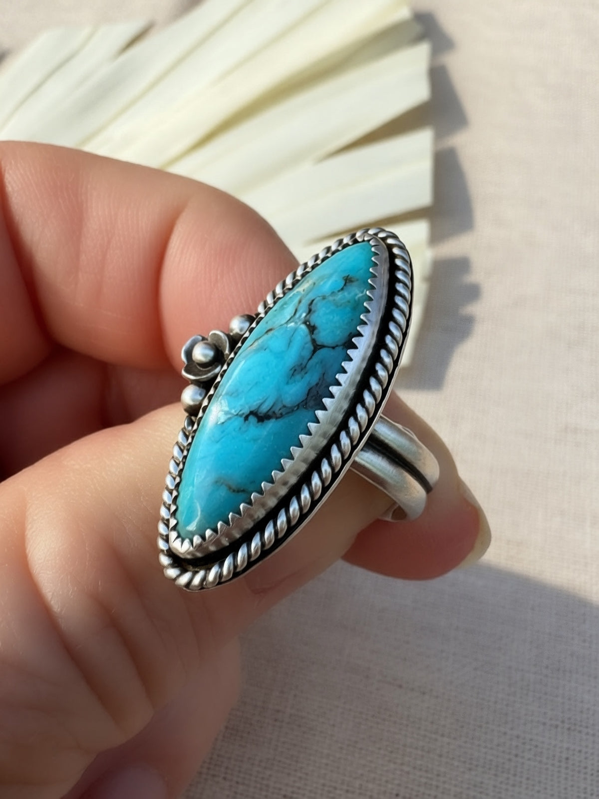 A sterling silver ring with a large oval turquoise stone held by a hand against a neutral fabric background.