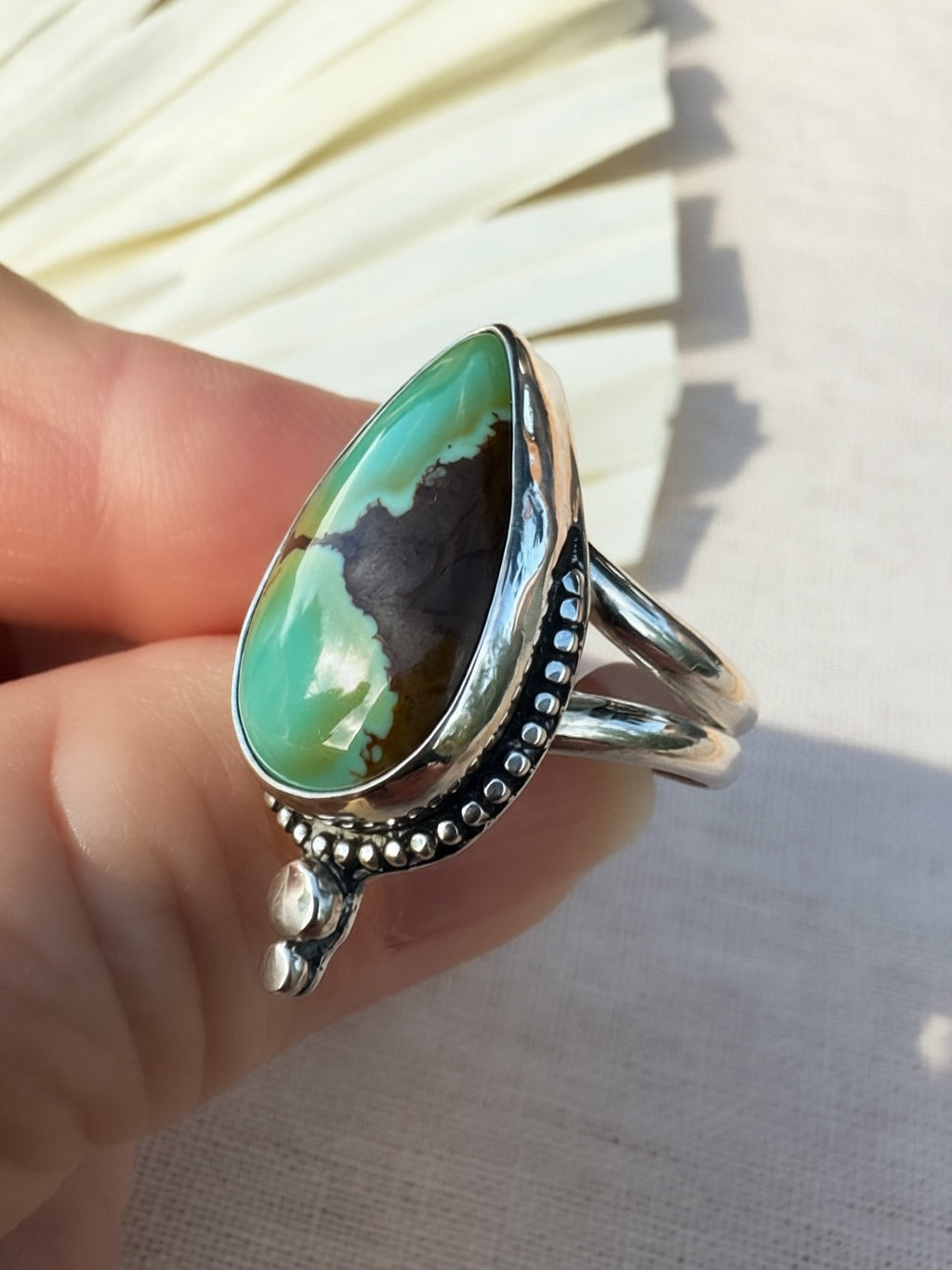 A sterling silver ring with a large teardrop-shaped turquoise stone being held.The ring features a polished silver band with decorative beaded detailing and a small silver accent below the main stone.