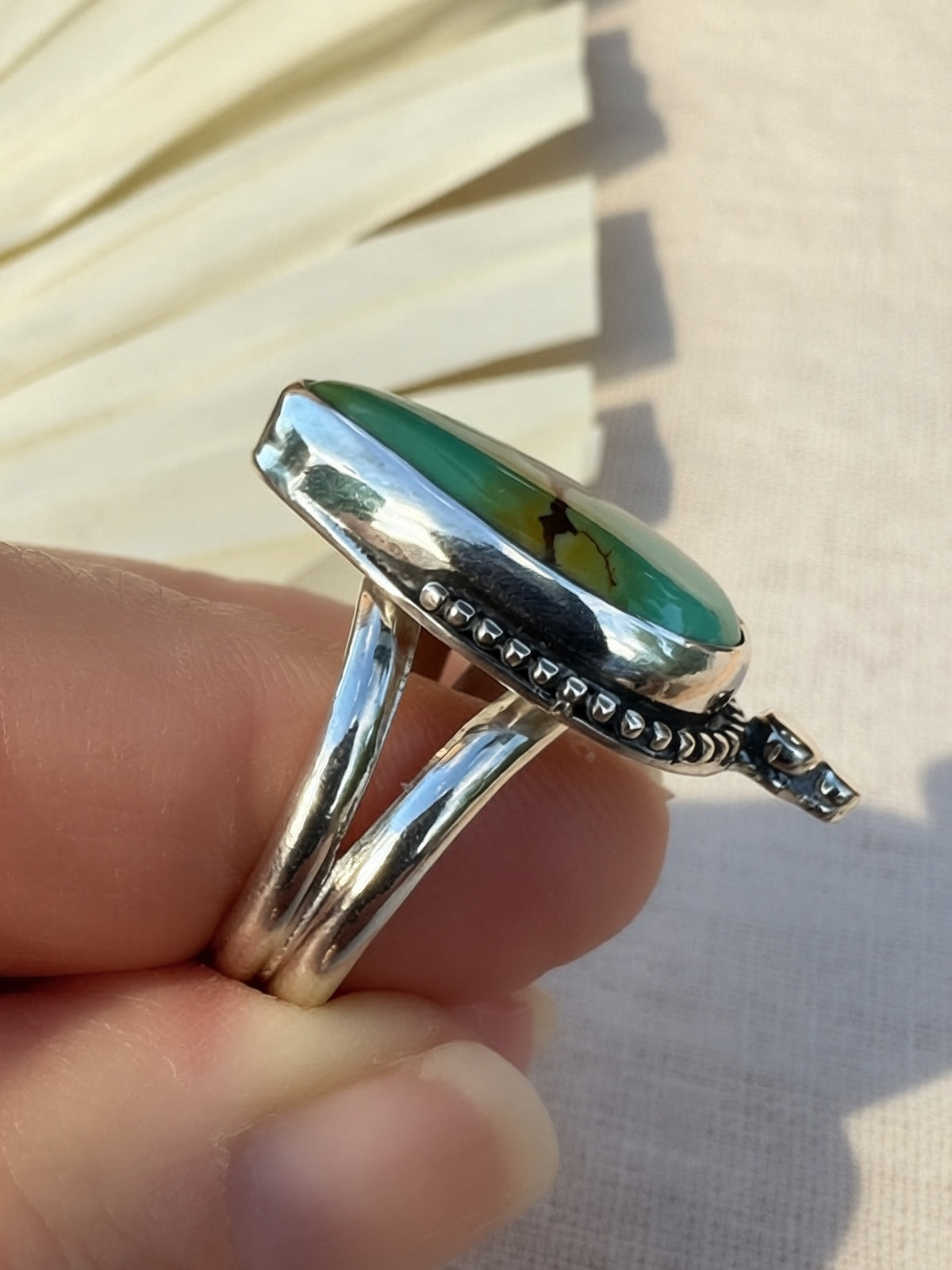 A sterling silver ring with an oval green stone held against a light beige fabric background.