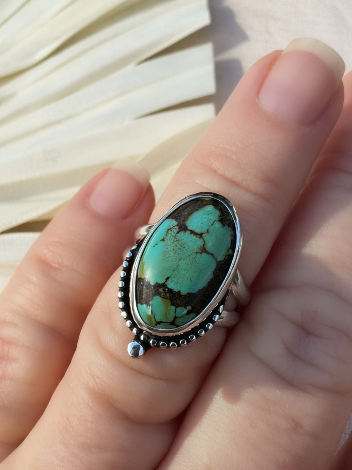 A close-up of a hand wearing a silver ring with a large oval turquoise stone featuring dark matrix veining.