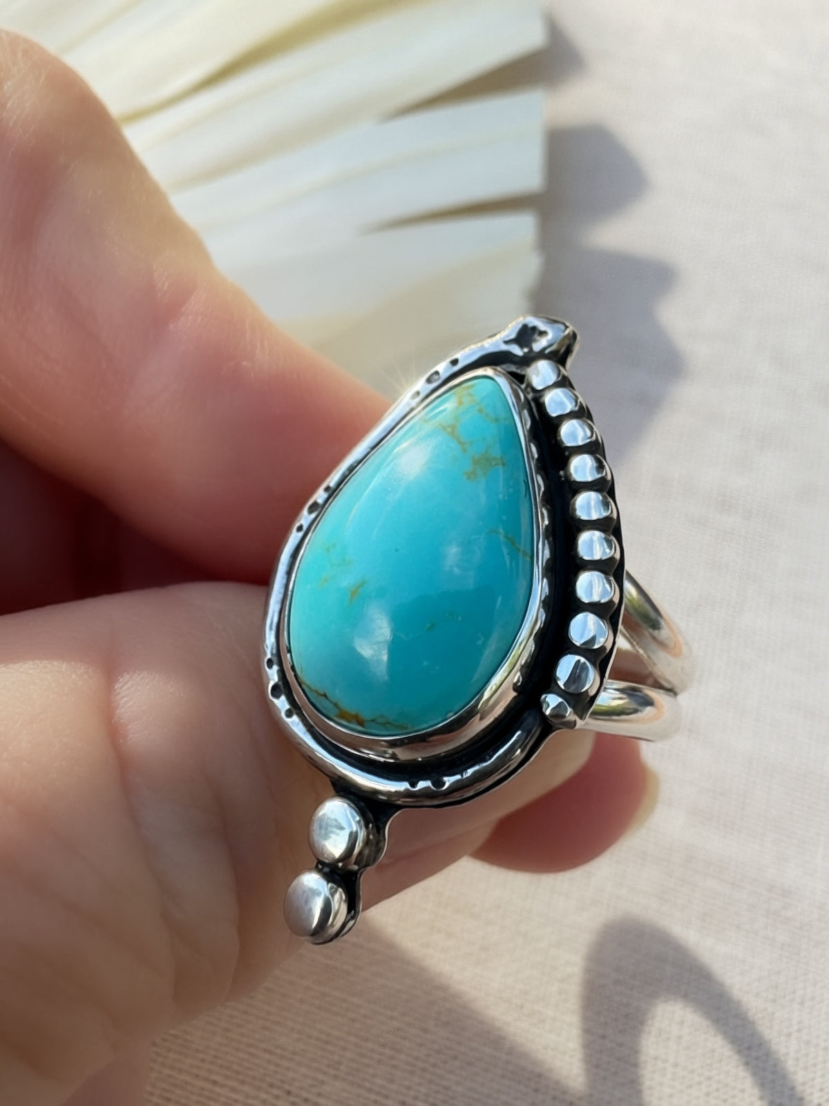 A sterling silver ring with a large turquoise stone held by a hand against a neutral beige background.