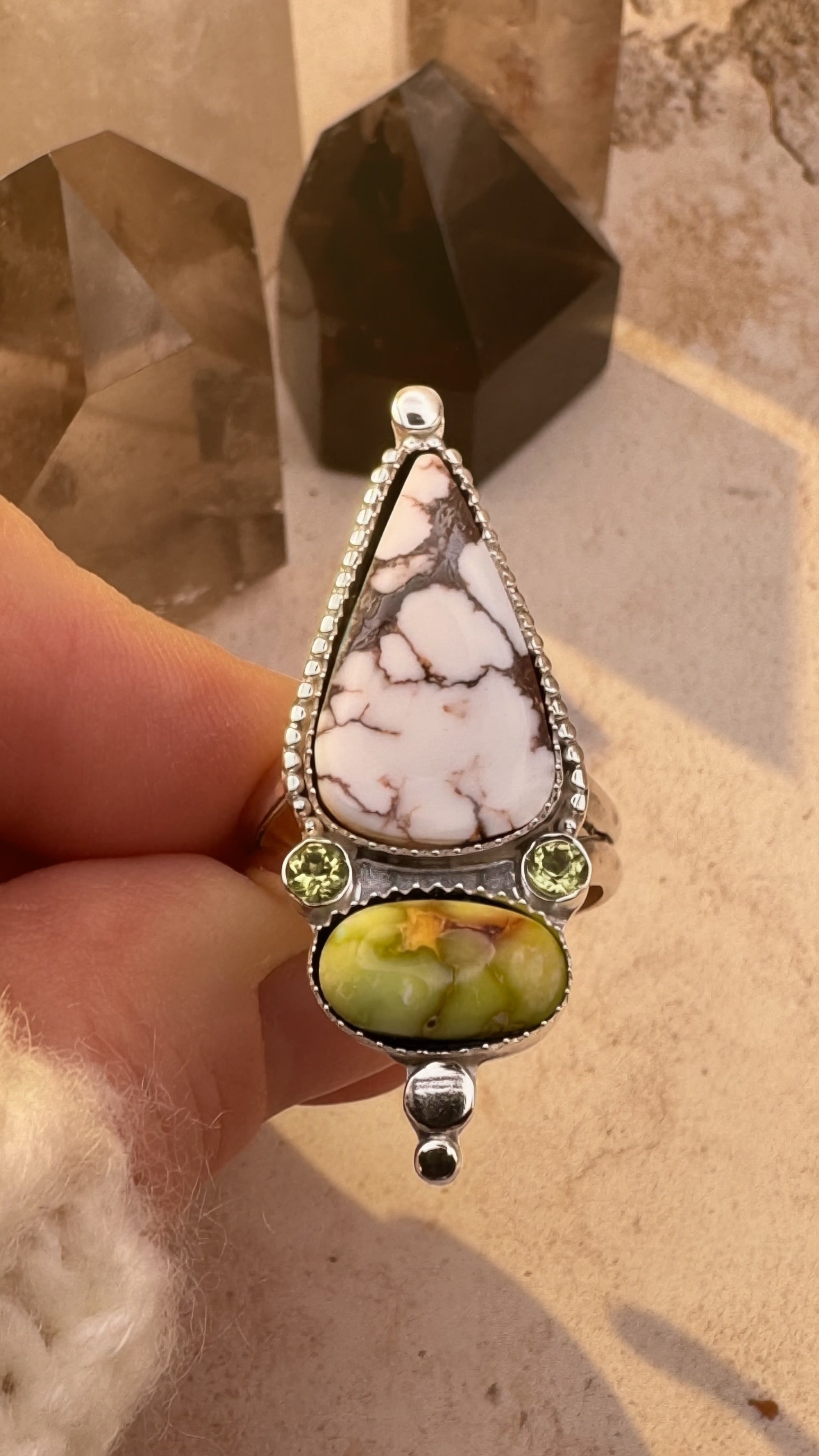 Large ring with featuring a green palomino stone and marbled white horse stone and 2 peridot gems, held by a hand.