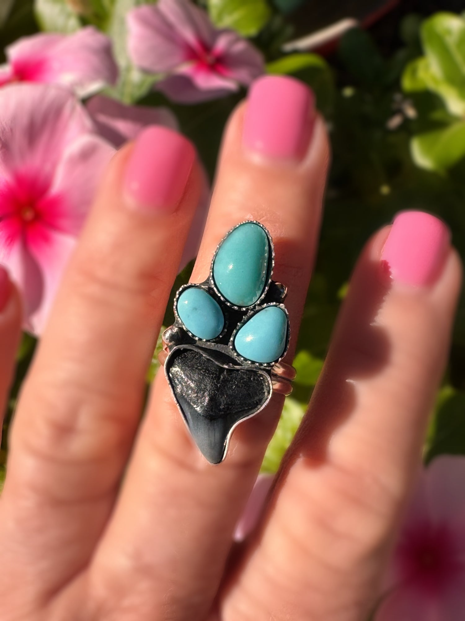 Turquoise stone ring on a finger with pink nail polish against a floral background