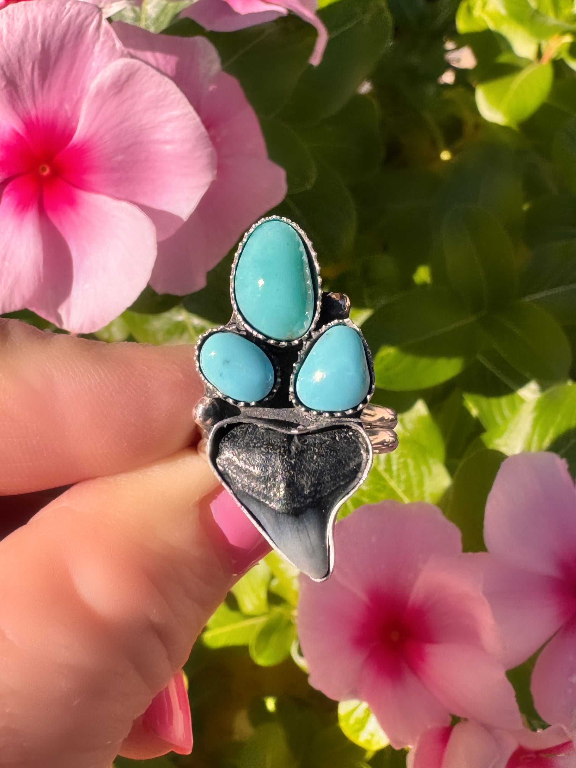Turquoise and shark tooth ring held in front of pink flowers