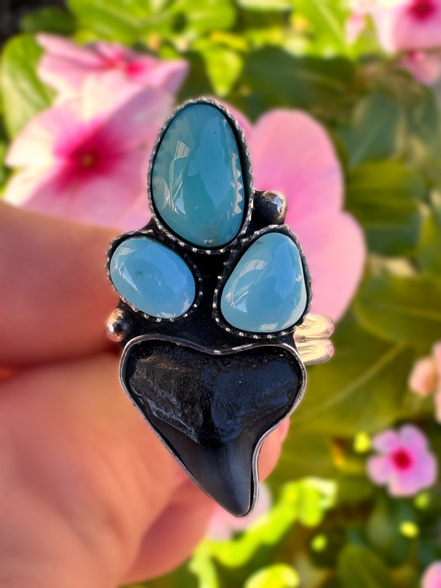 Ring with blue stones and shark tooth design held against a floral background