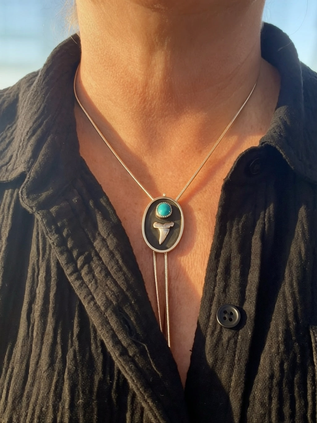Necklace with a pendant featuring a Bisbee turquoise stone and silver shark tooth worn by a person.