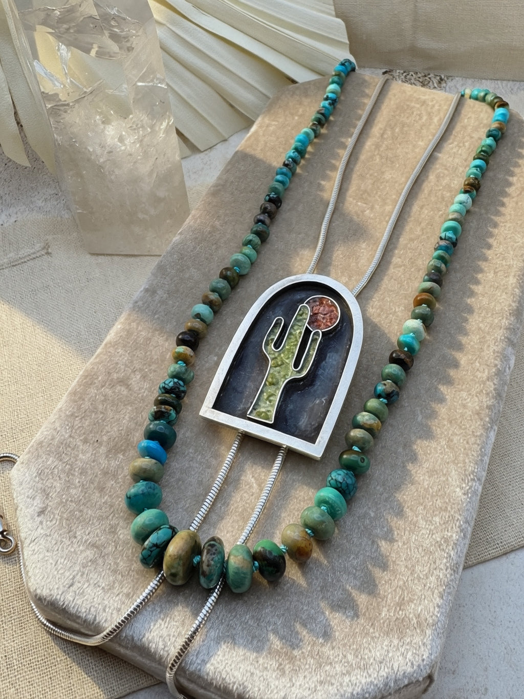 Turquoise hand knotted beaded Necklace with a cactus and sun bolo necklace on a textured surface