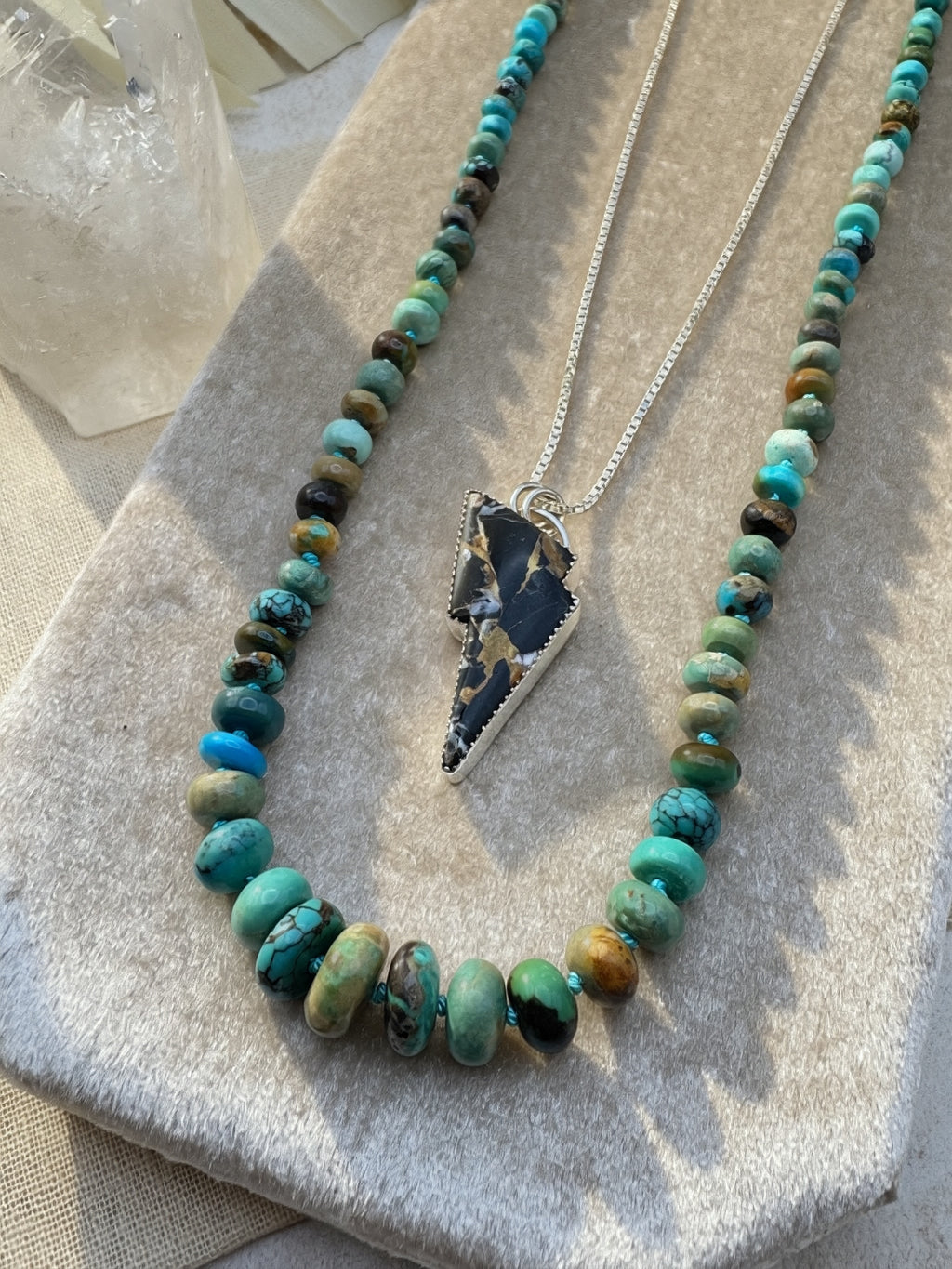 Necklace stack with turquoise beads and a lightning bold pendant on a textured surface