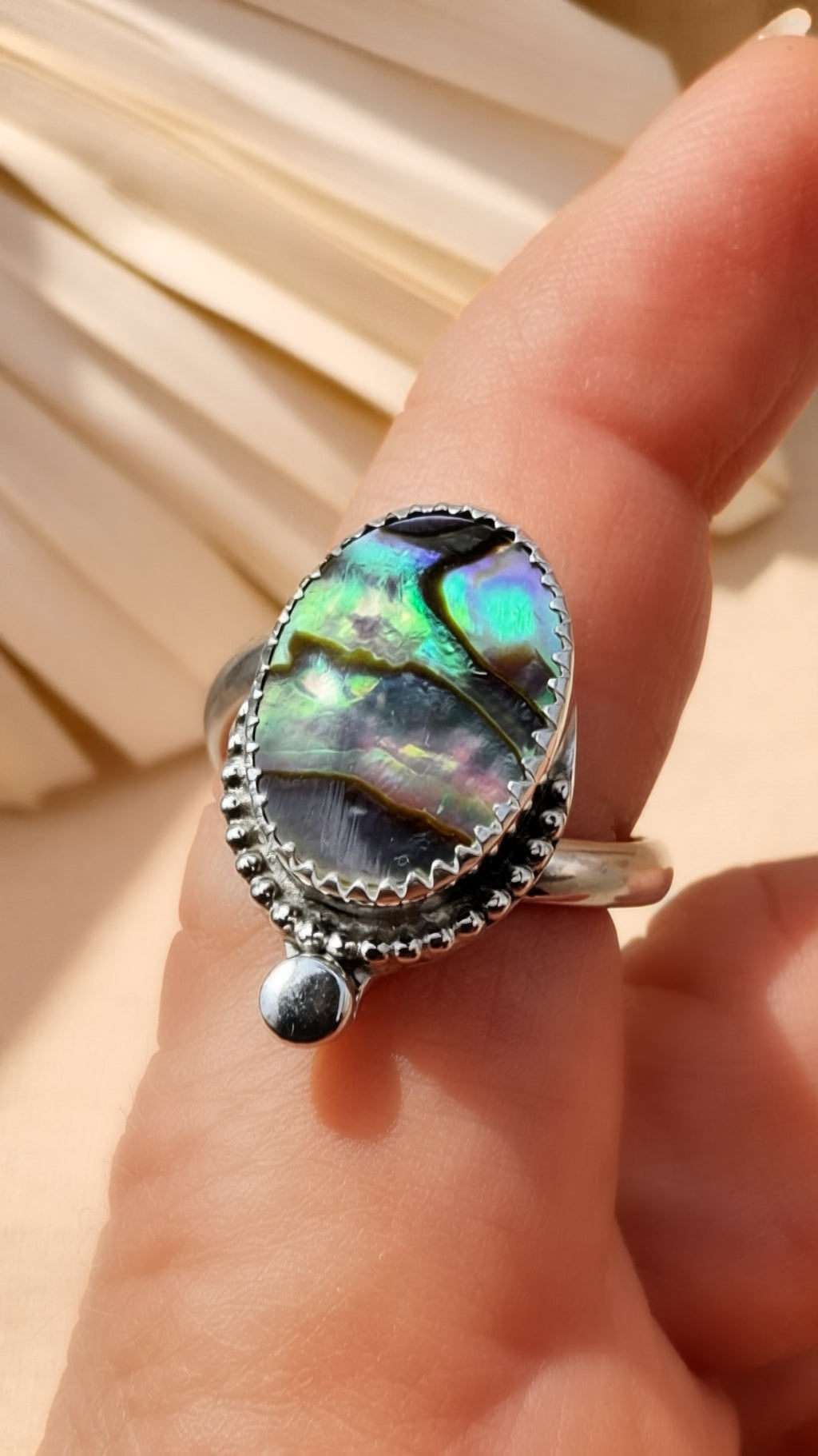 Ring with an abalone shell on a hand against a neutral background