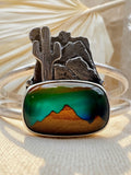 Close-up of handcrafted silver cuff showing detailed hand-sawed desert landscape with oxidized texture, landscape triplet stone