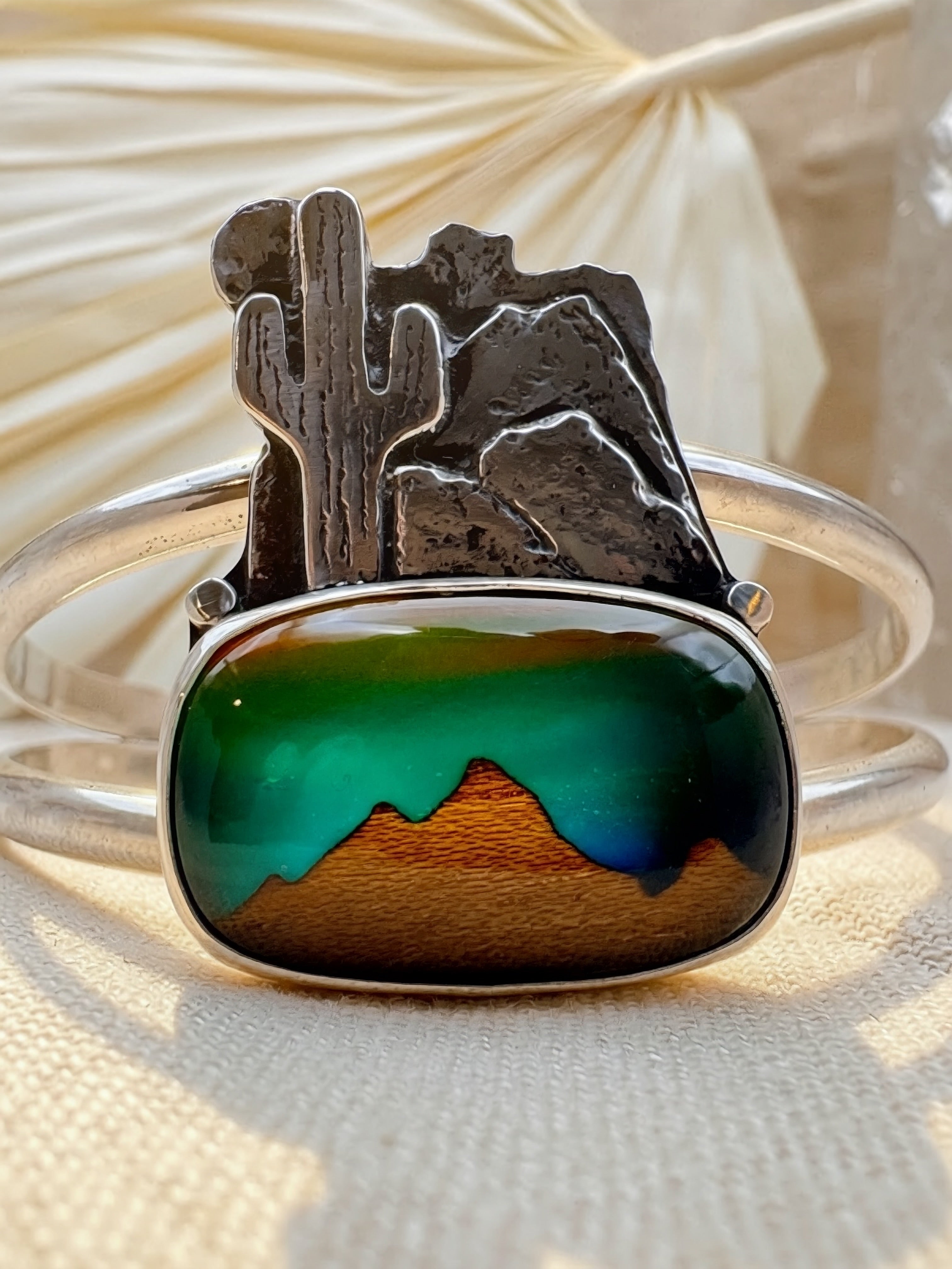 Close-up of handcrafted silver cuff showing detailed hand-sawed desert landscape with oxidized texture, landscape triplet stone